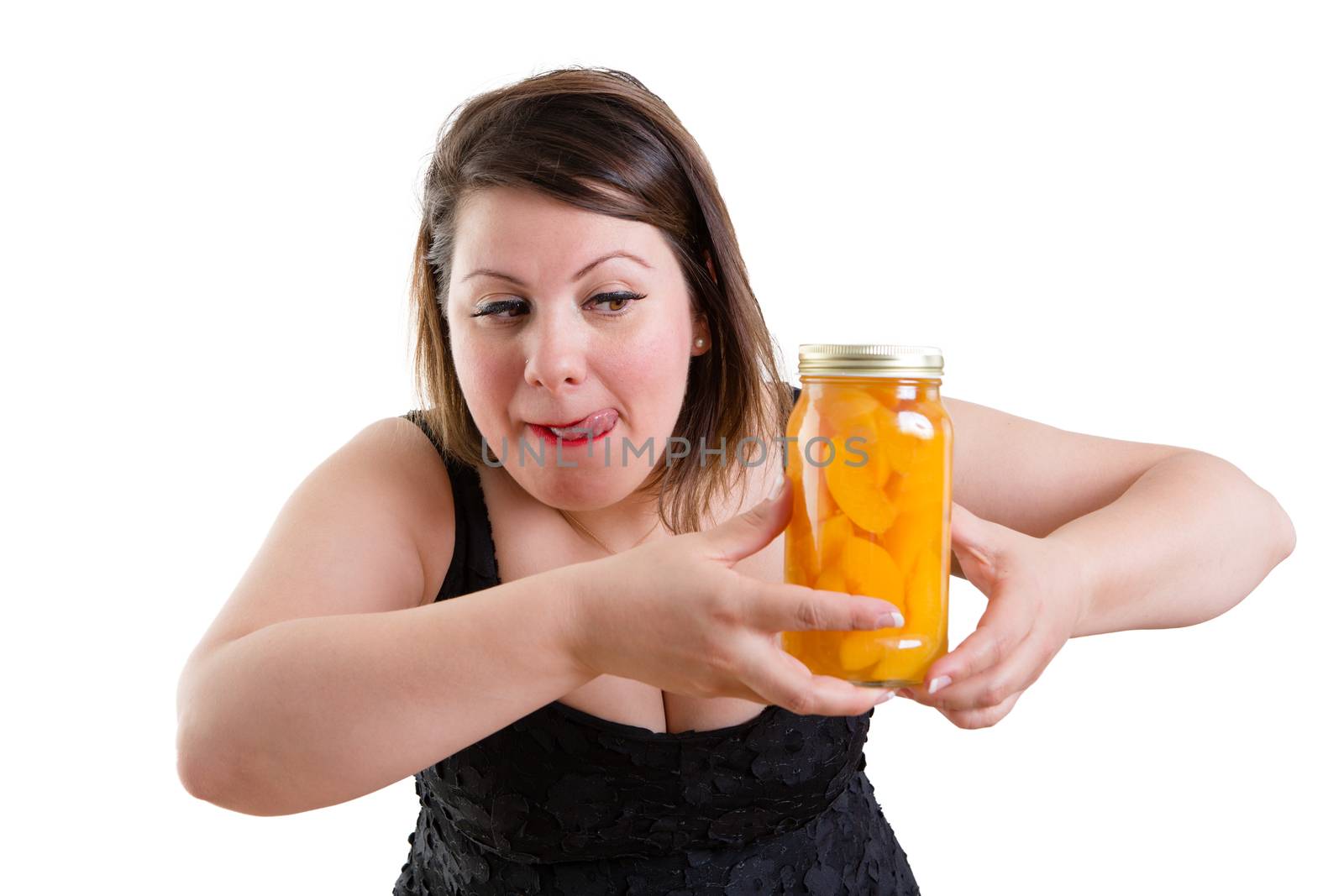 Plump woman licking her lips in anticipation as she eyes a jar of appetizing tempting homemade peaches she is holding in her hand in a health, nutrition and diet concept, isolated on white