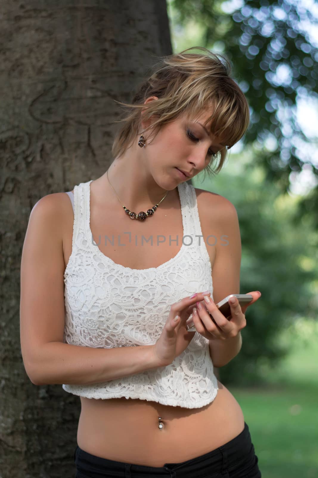 Attractive blonde young woman outdoors using cell phone, typing and sending messages