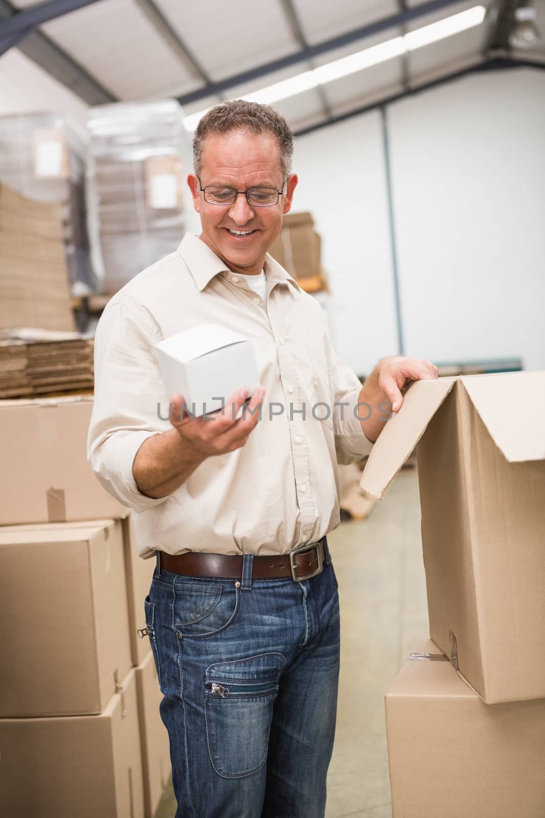 Smiling warehouse worker holding small box in a large warehouse
