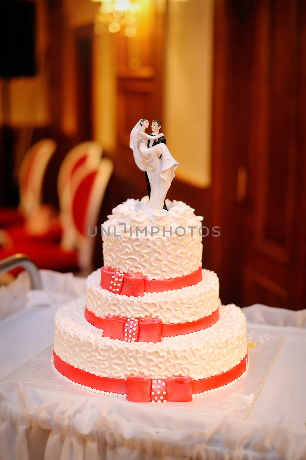 three-tiered white wedding cake with red ribbons.
