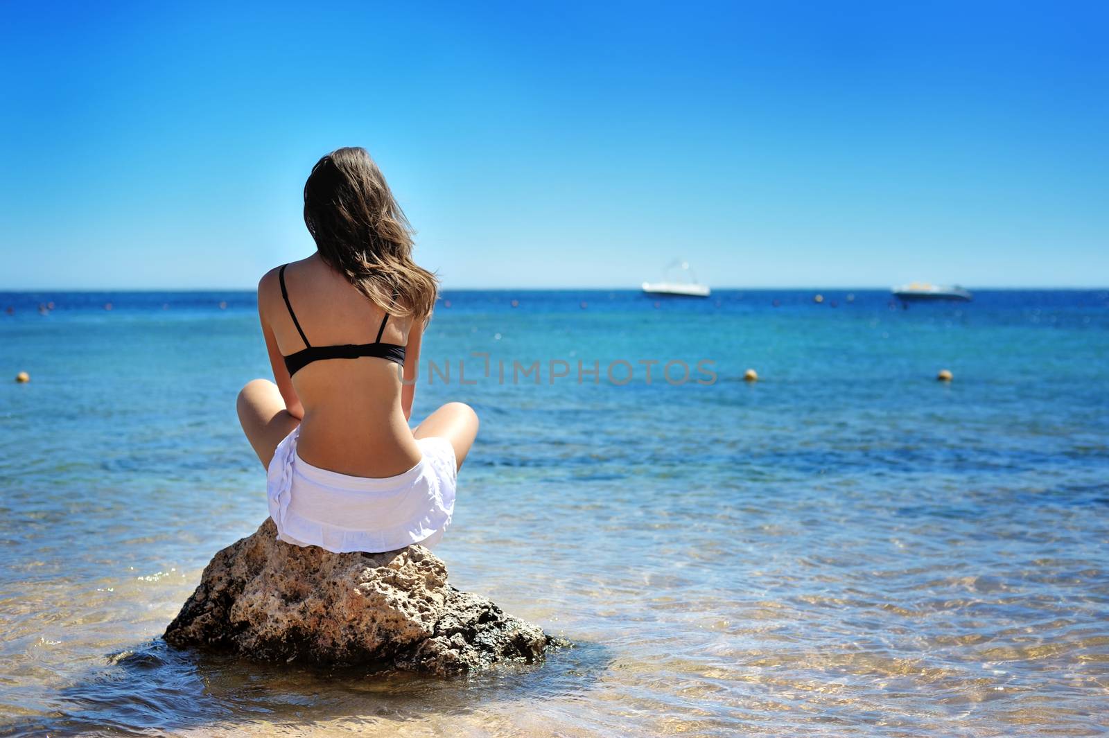 Young woman sitting on sand and looking to a sea.