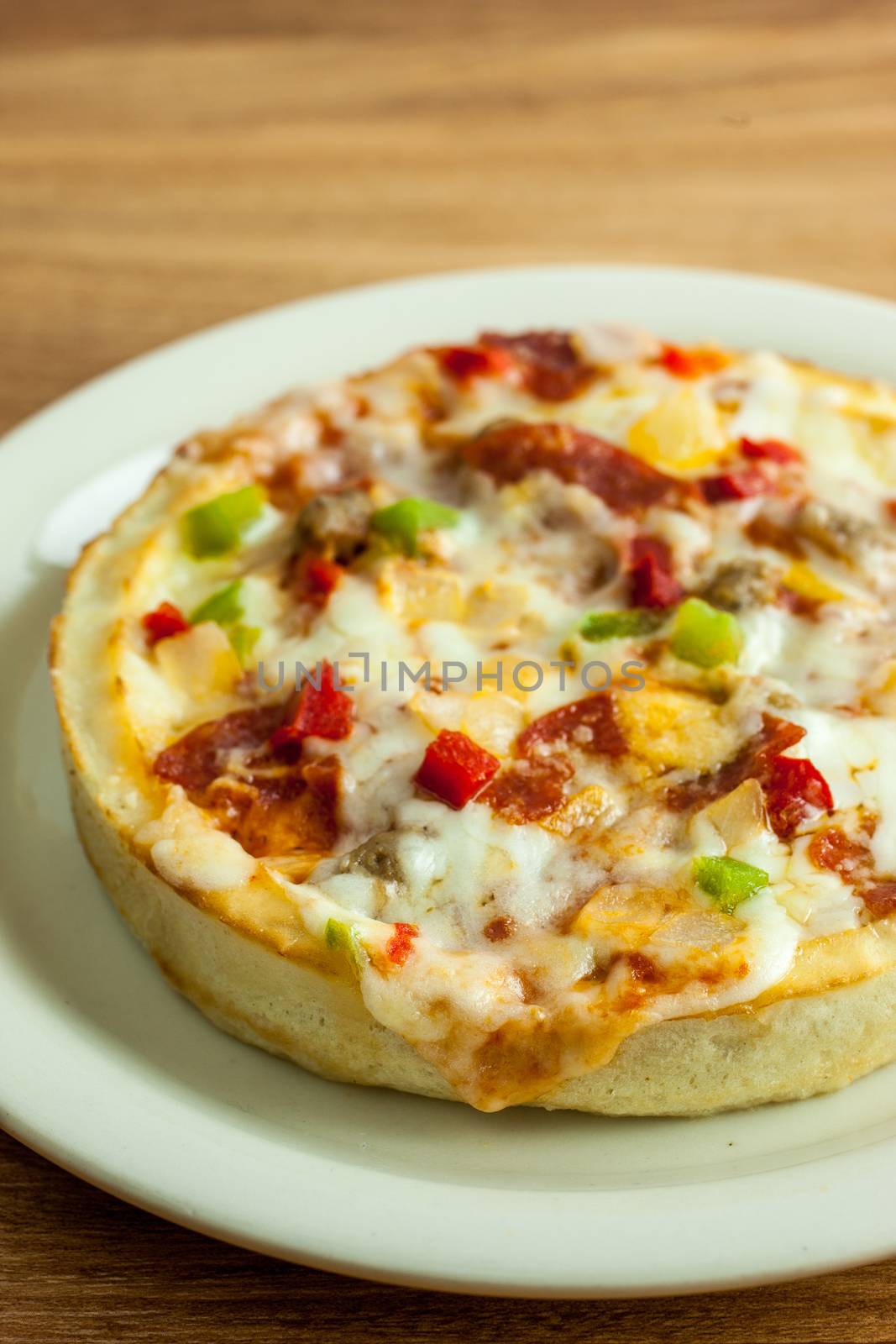 A personal sized deep dish pizza on a white plate, sitting on a wooden table.