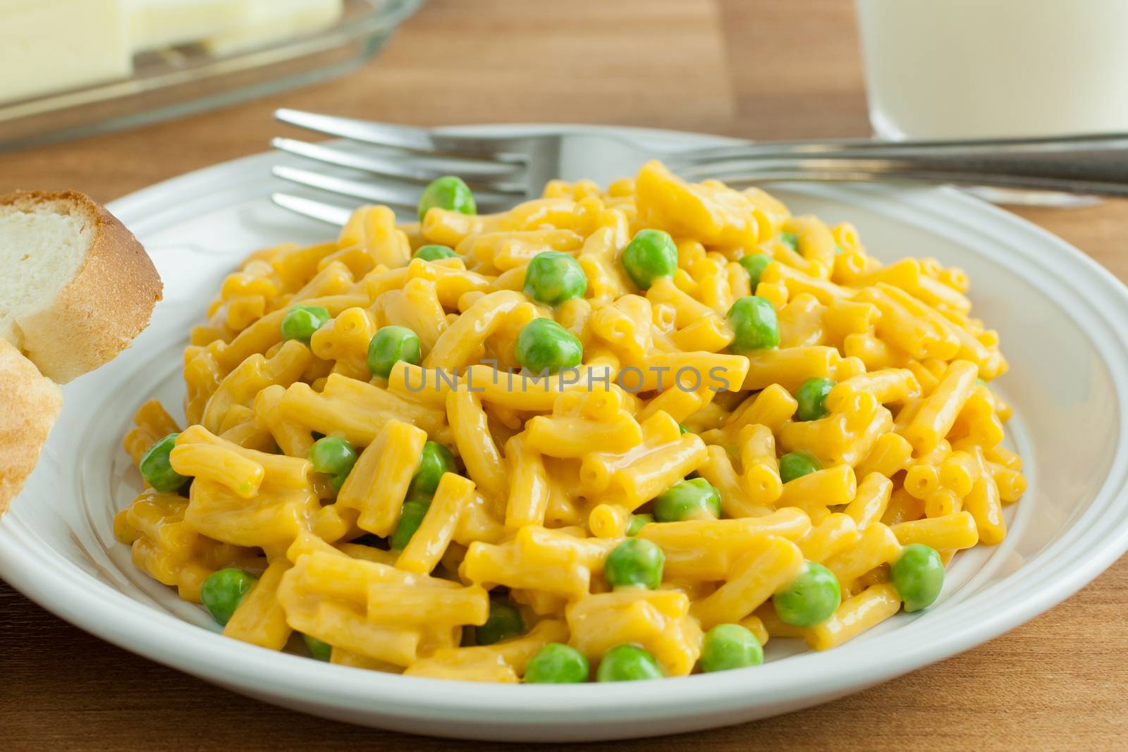 Macaroni and chesse dinner with peas, a slice of bread and butter, and a glass of milk.