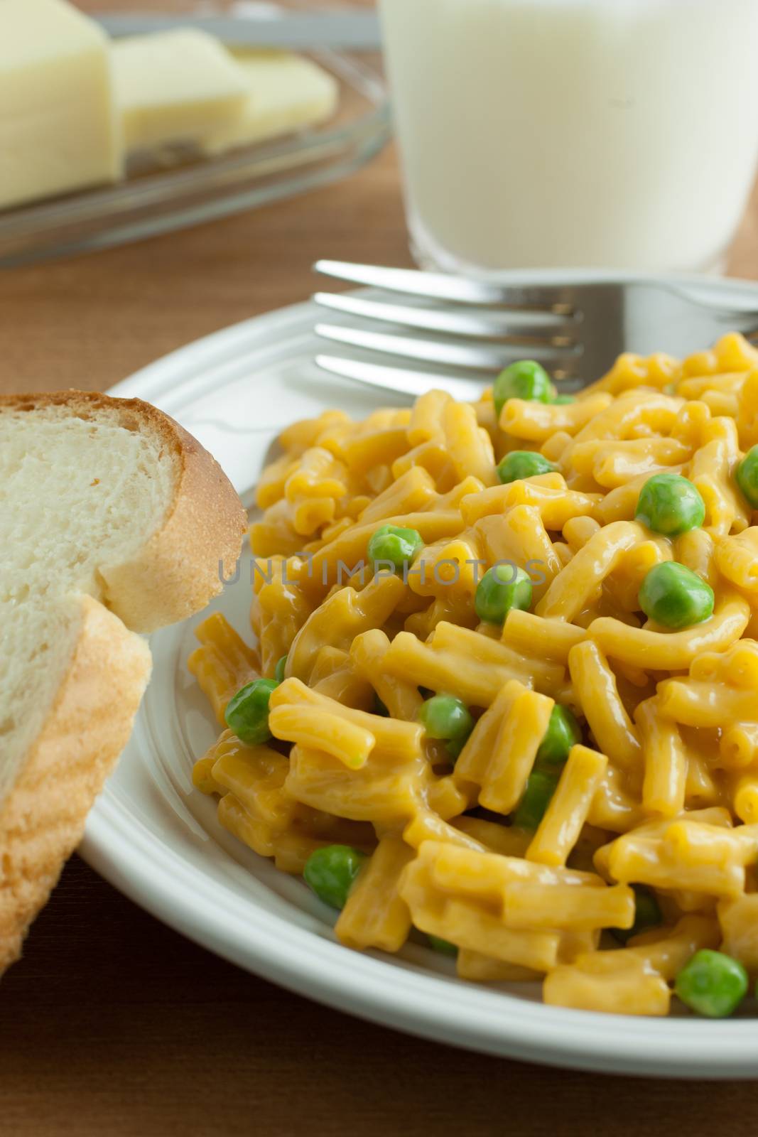 Macaroni and chesse dinner with peas, a slice of bread and butter, and a glass of milk.