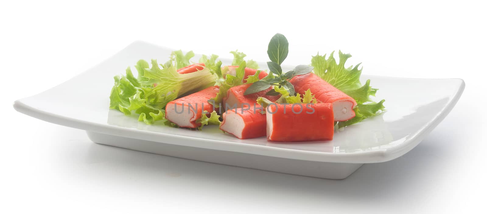 Salad with pieces of red crab stick, fresh lettuce and basil on the white plate