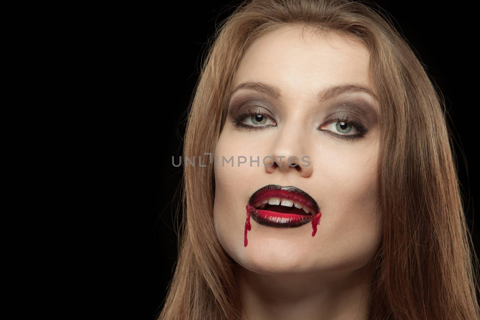 Close-up portrait of a smiling gothic vampire woman on a black background