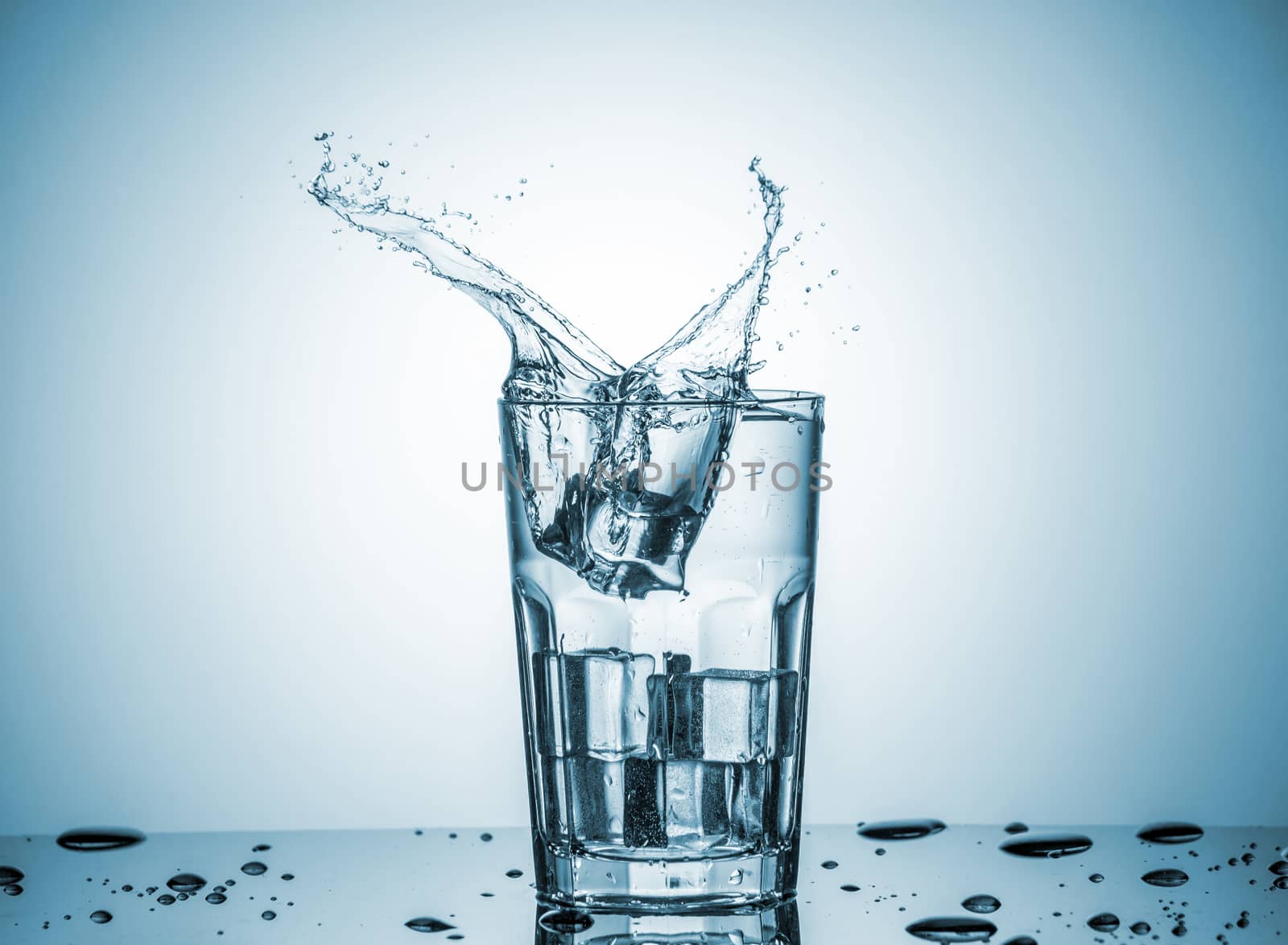 ice cubes falling into a glass of water on blue background