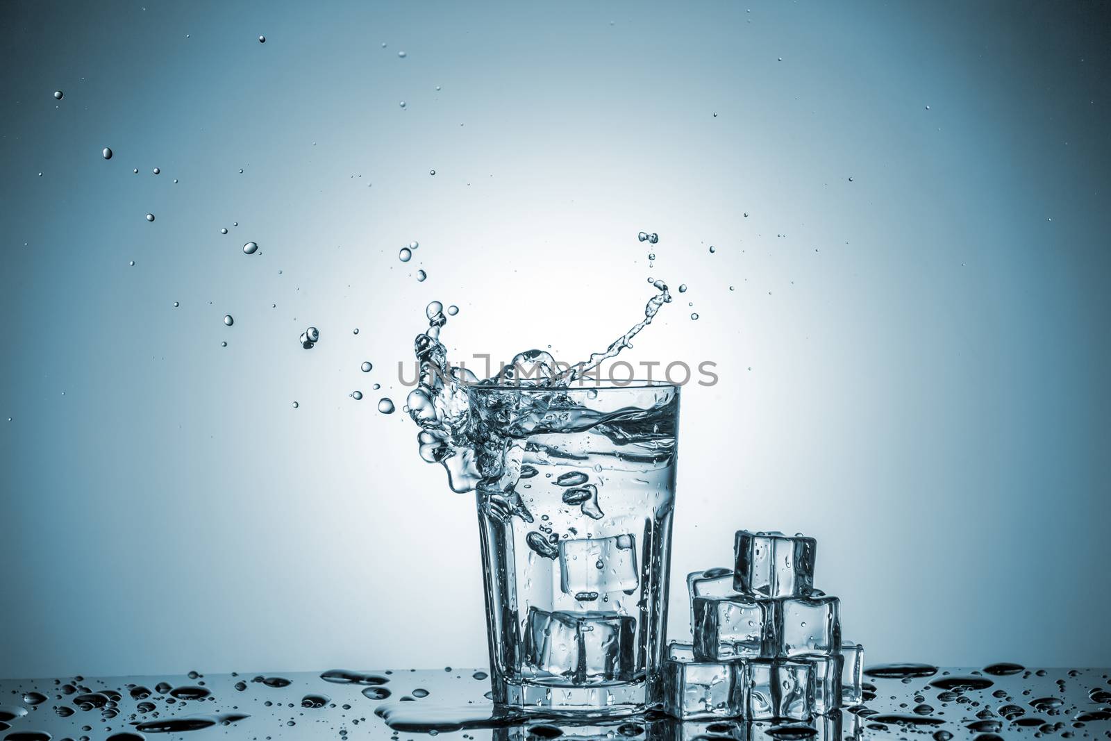 ice cubes falling into a glass of water and ice cubes, lying next, on blue background