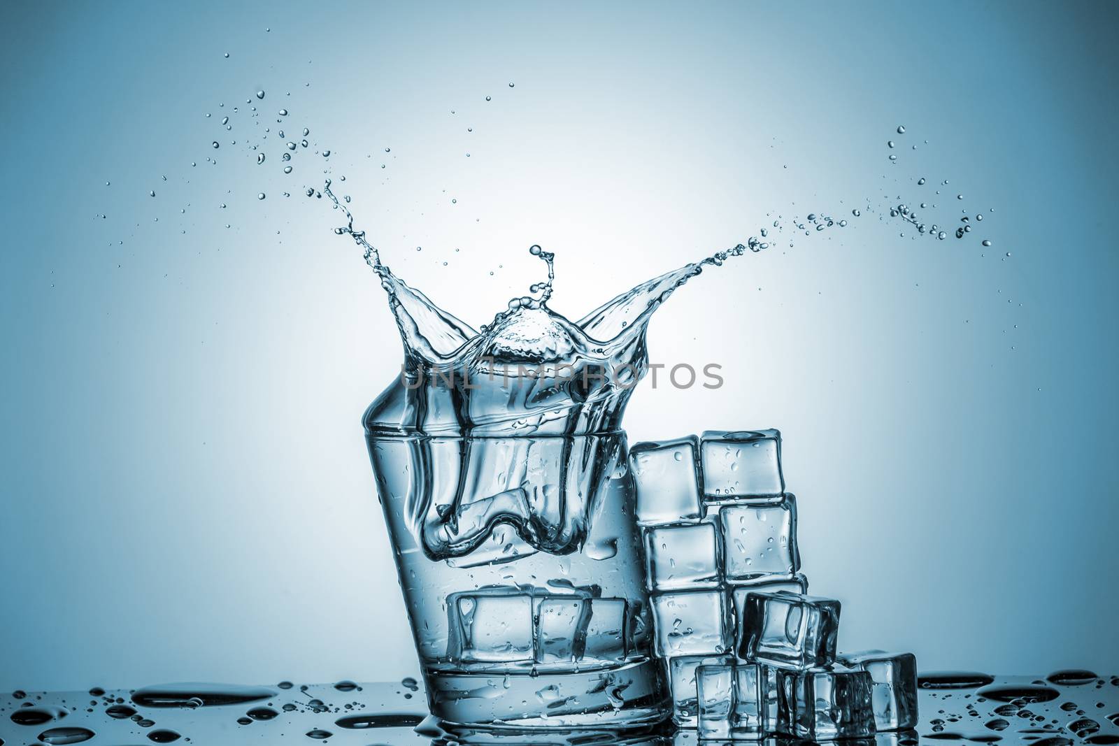 ice cubes falling into a glass of water and ice cubes, lying next, on blue background