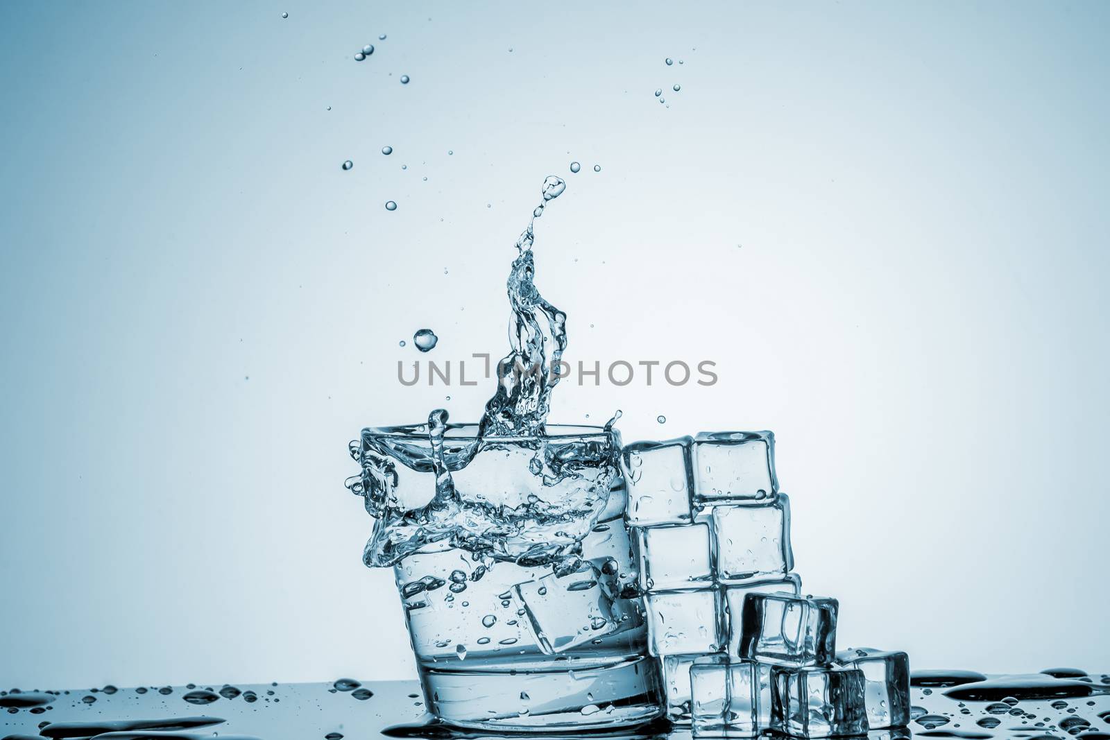 ice cubes falling into a glass of water and ice cubes, lying next, on blue background