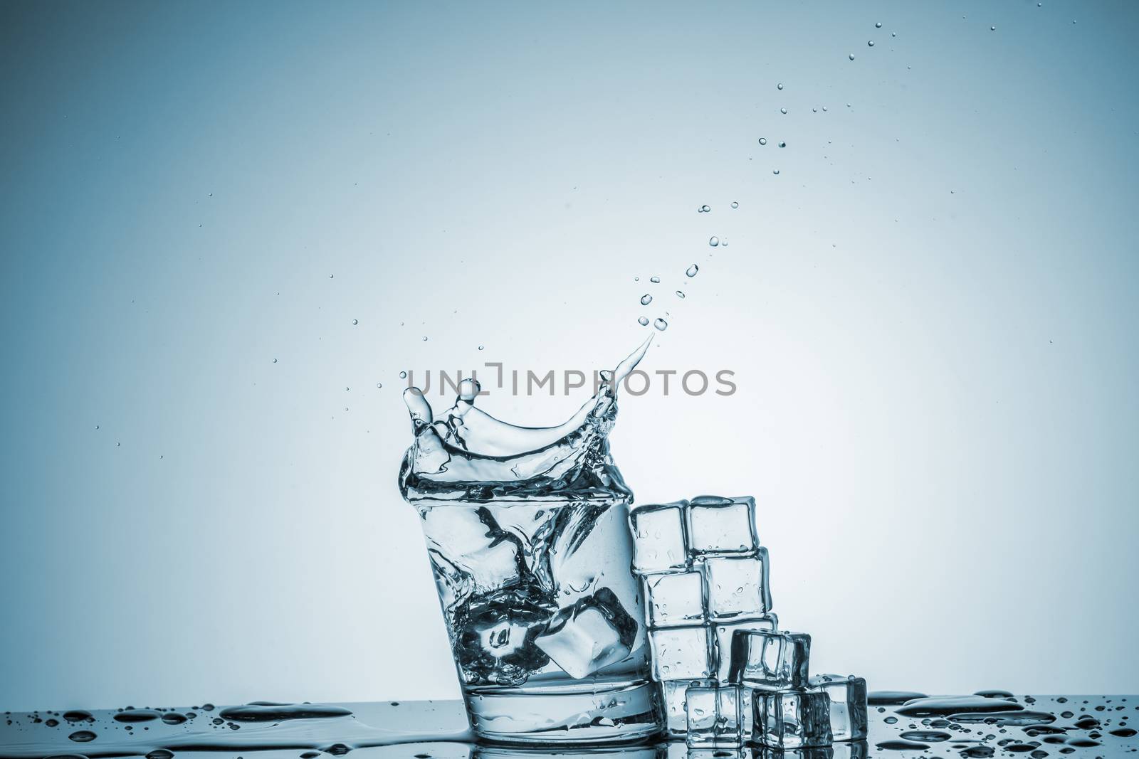 ice cubes falling into a glass of water and ice cubes, lying next, on blue background