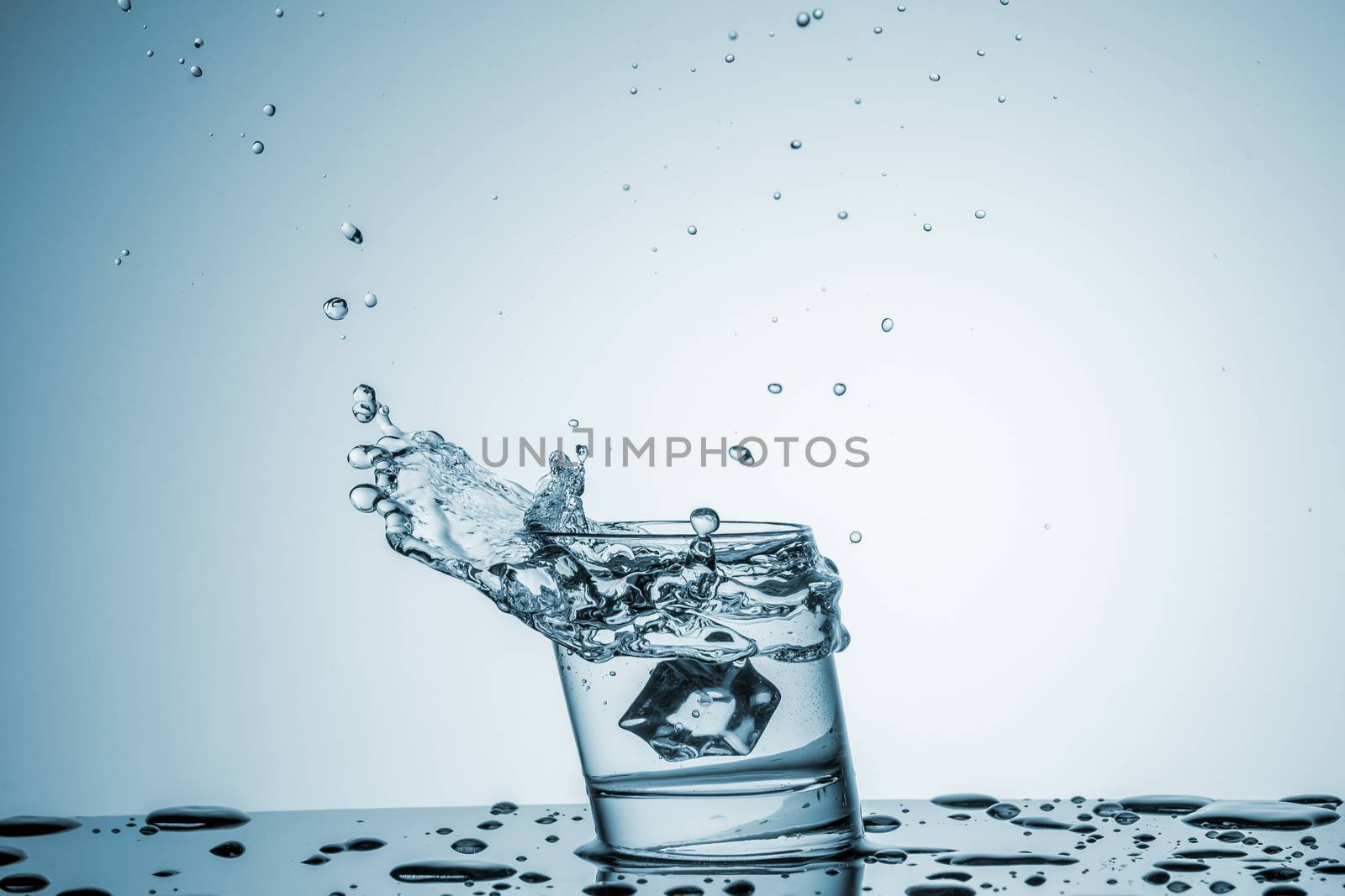 ice cube falling into a glass of water on blue background