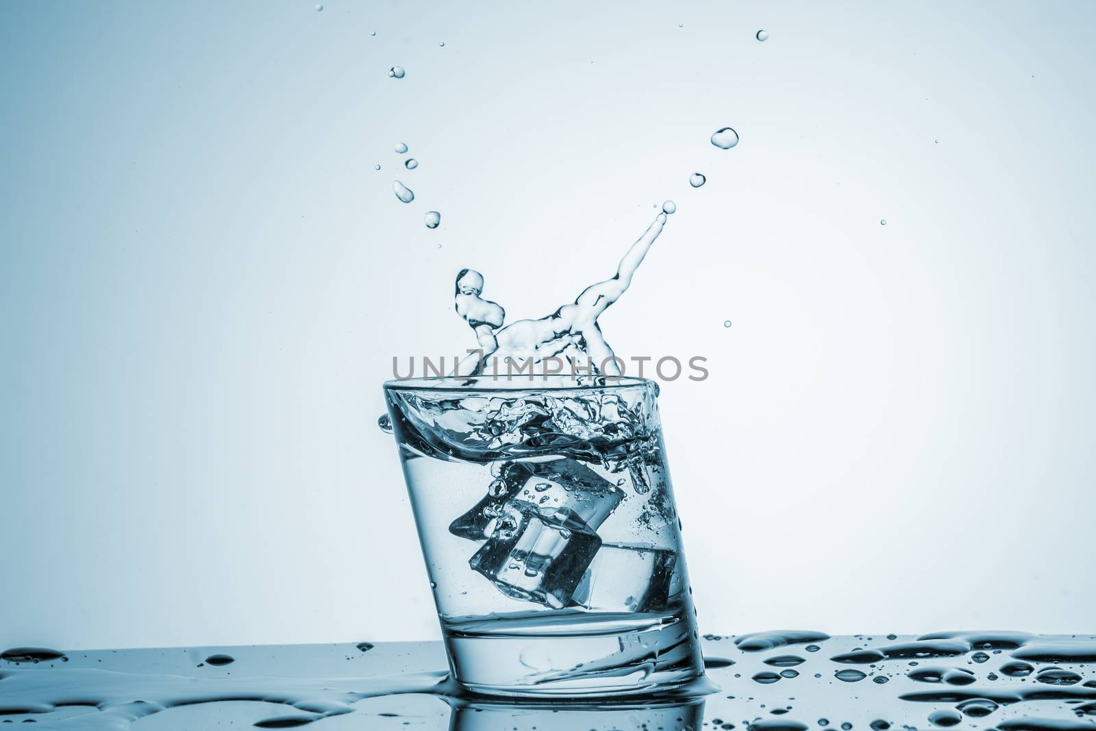 ice cube falling into a glass of water on blue background