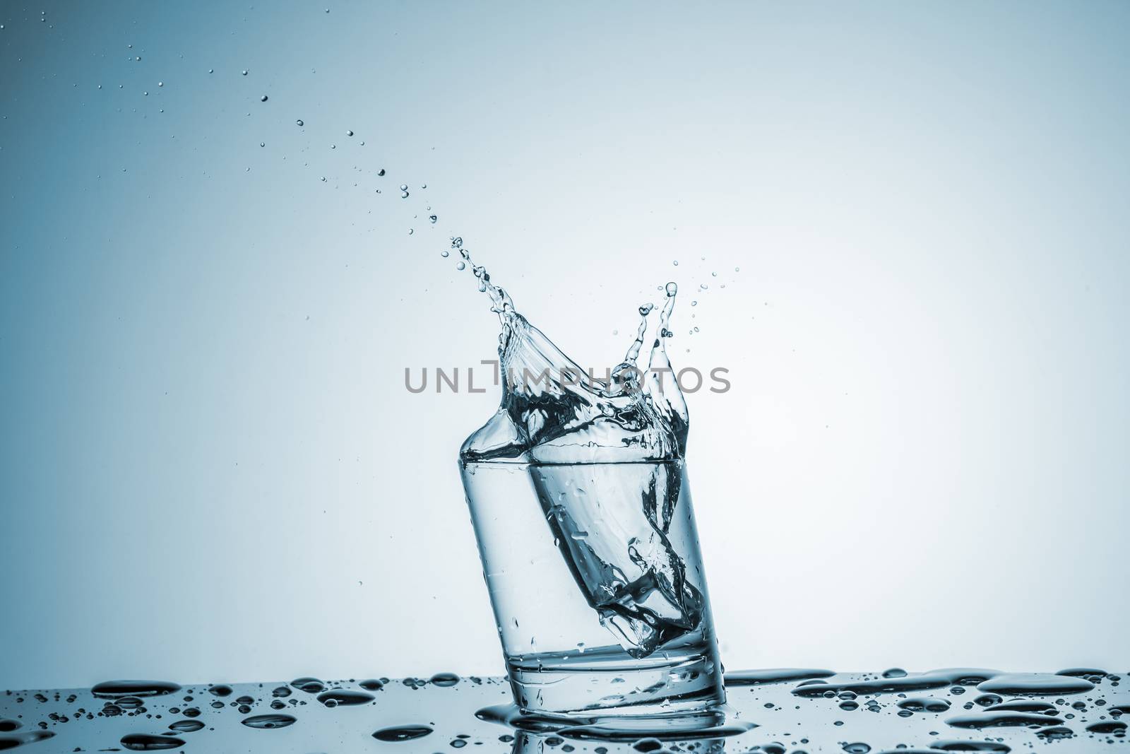 ice cube falling into a glass of water on blue background