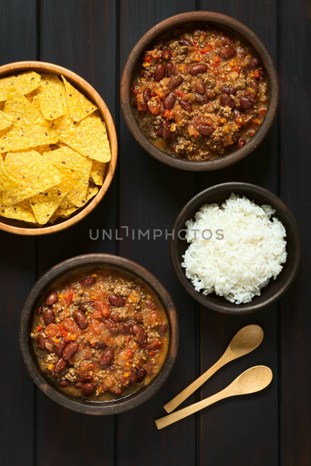 Overhead shot of two bowls of chili con carne with rice and tortilla chips, photographed on dark wood with natural light