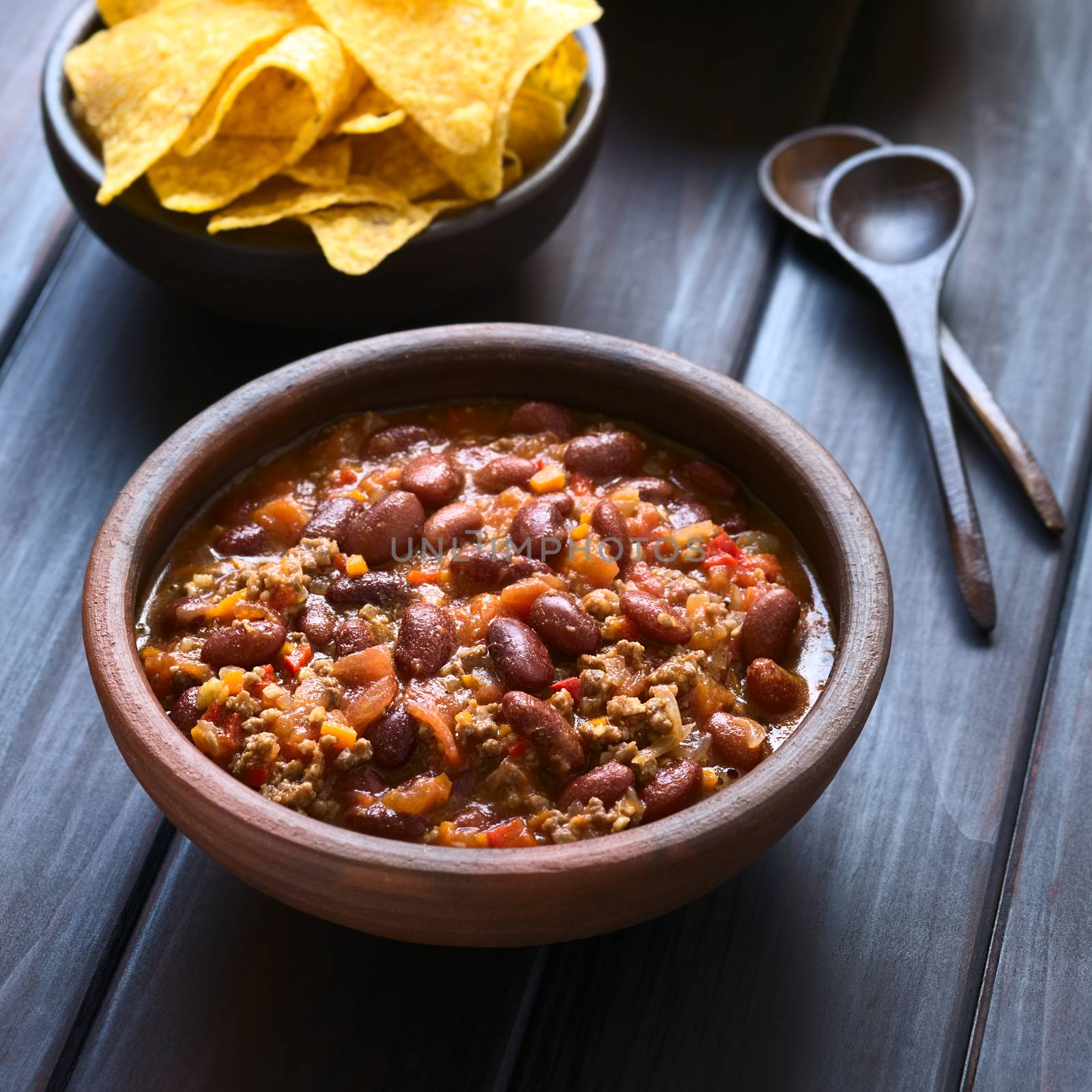 Rustic bowl of chili con carne with tortilla chips in the back, photographed with natural light (Selective Focus, Focus in the middle of the chili)