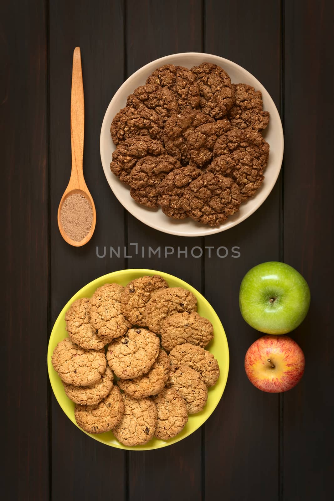 Overhead shot of chocolate and apple oatmeal cookies on plates, photographed on dark wood with natural light
