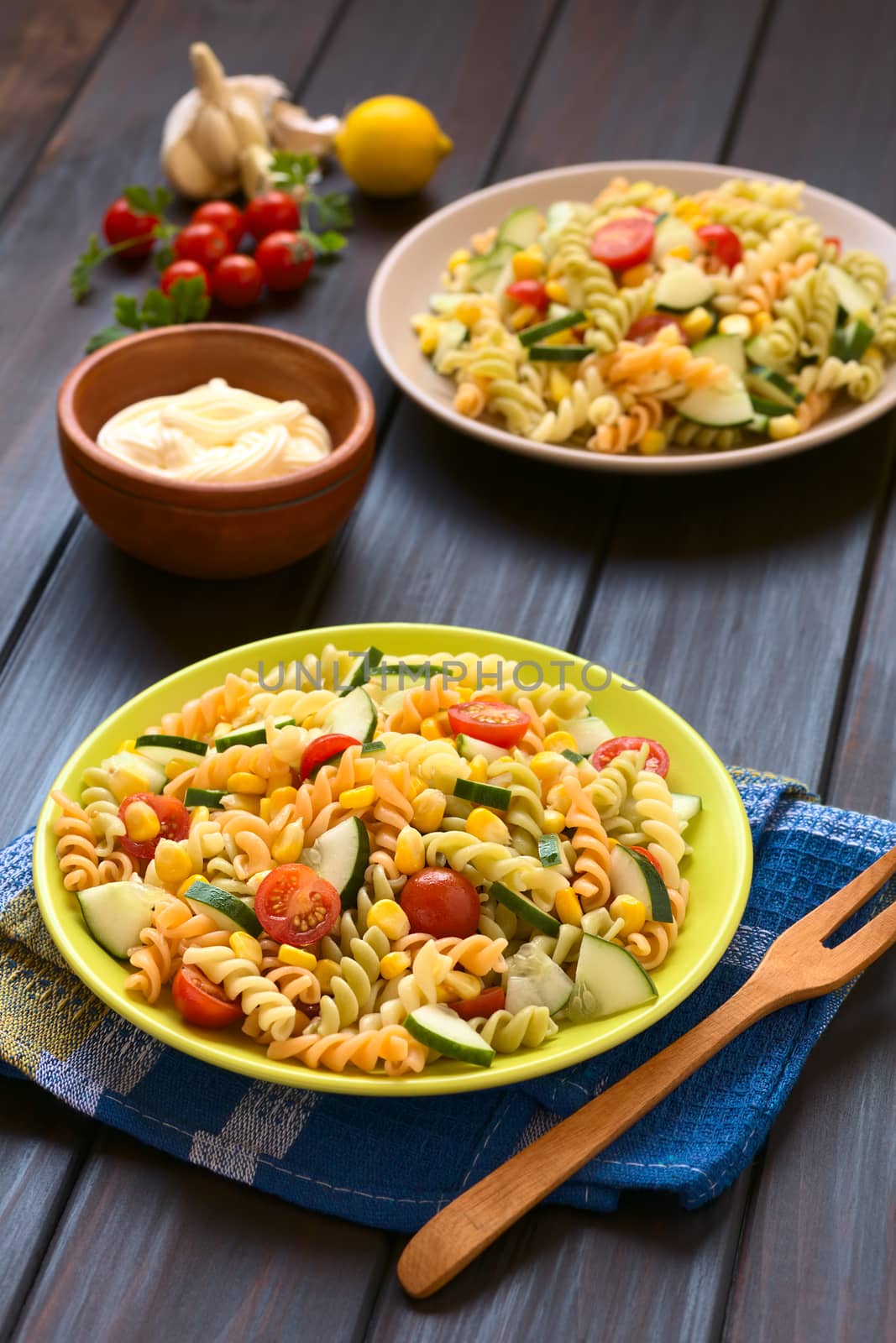 Two plates of vegetarian pasta salad made of tricolor fusilli, sweet corn, cucumber and cherry tomato with mayonnaise in the back, photographed with natural light (Selective Focus, Focus one third into the first salad) 