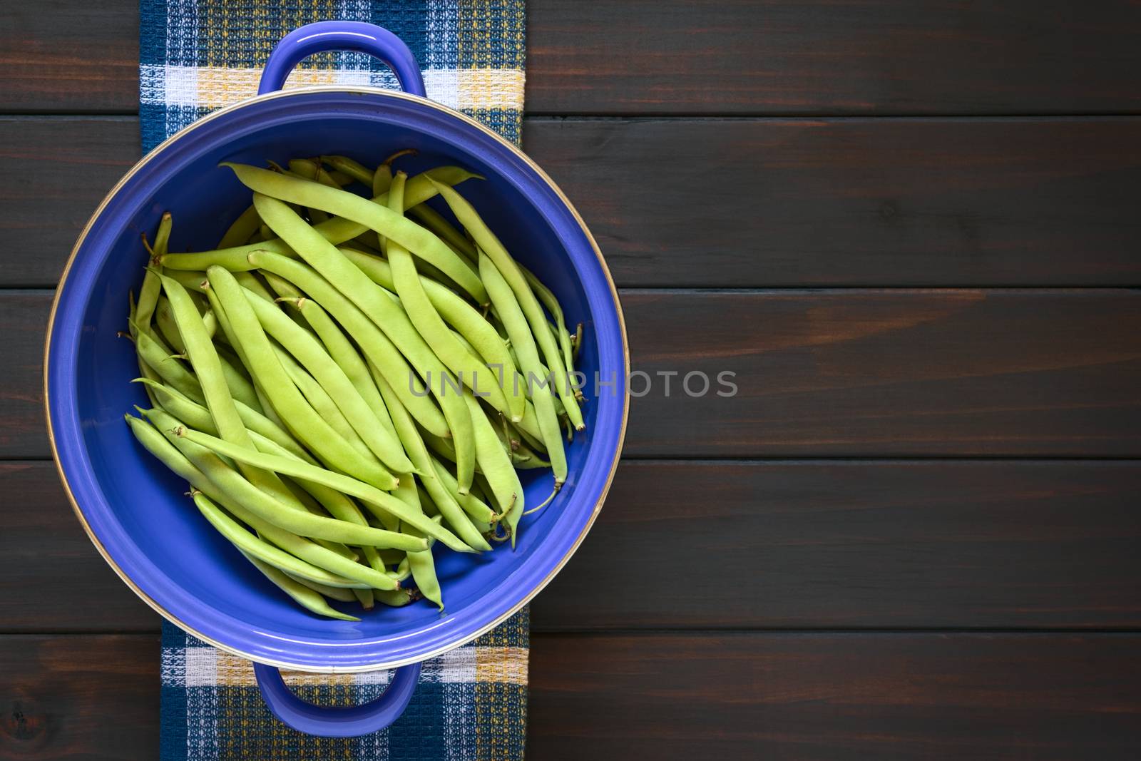 Overhead shot of green beans in blue metal strainer, photographed on dark wood with natural light