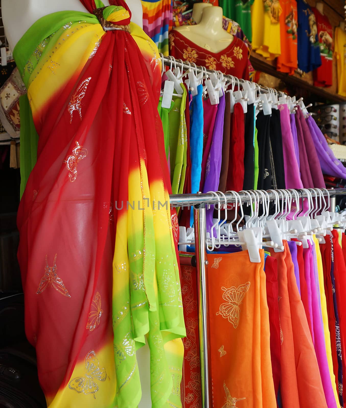 Rows of colourful clothes hanging at market  by ninun