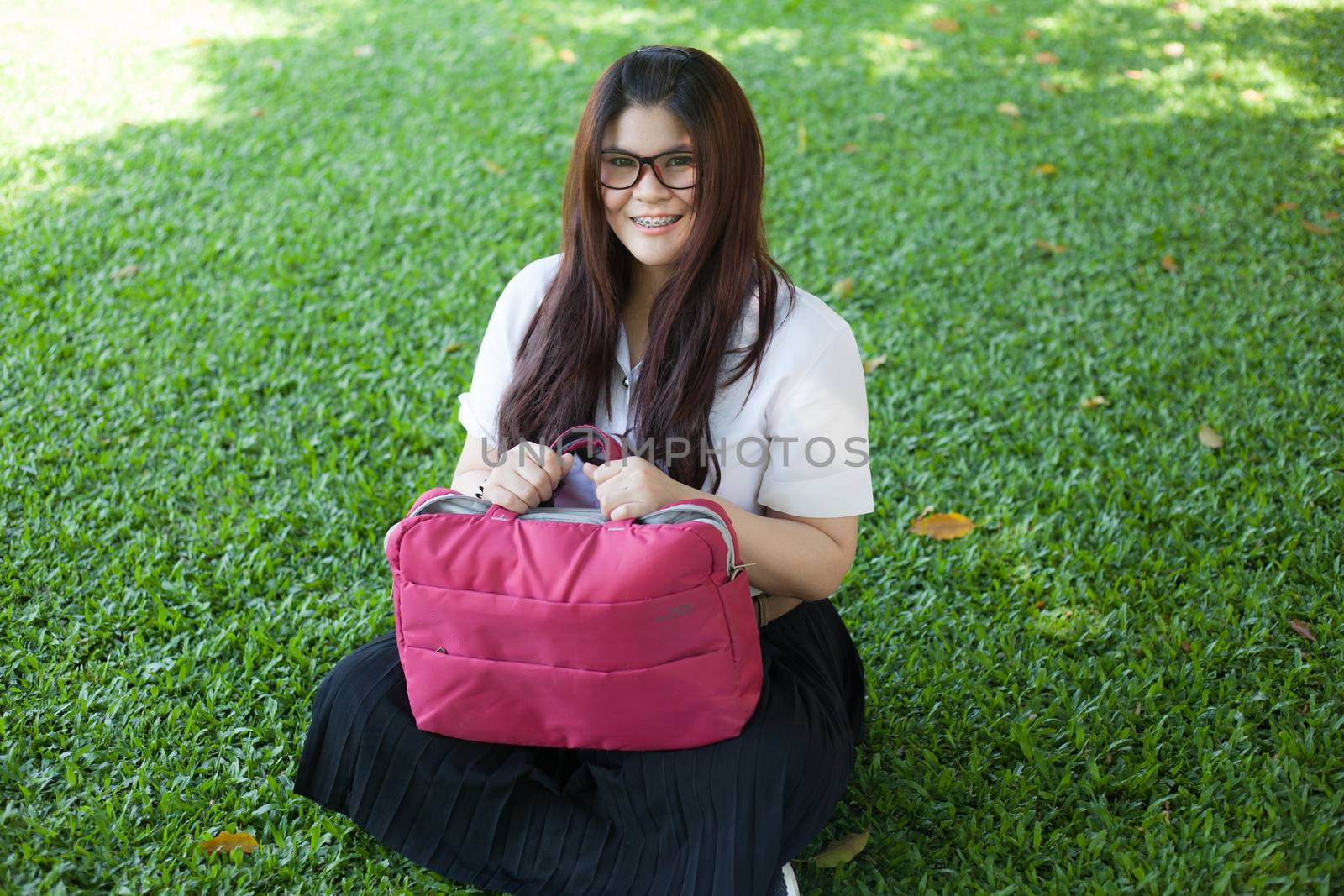 Female student sitting on the lawn. Pink bag was placed on it.