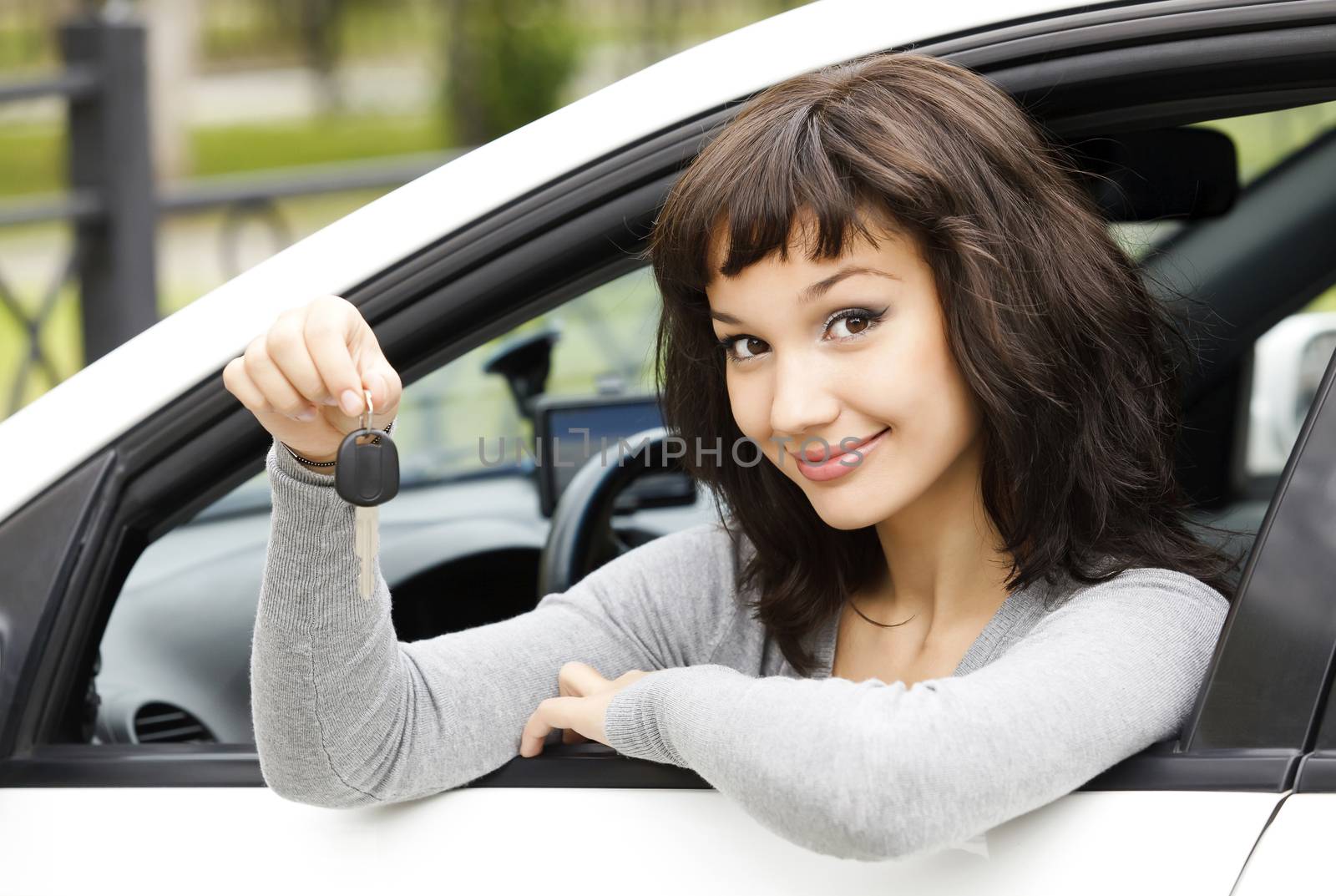 Pretty female driver in a white car showing the car key