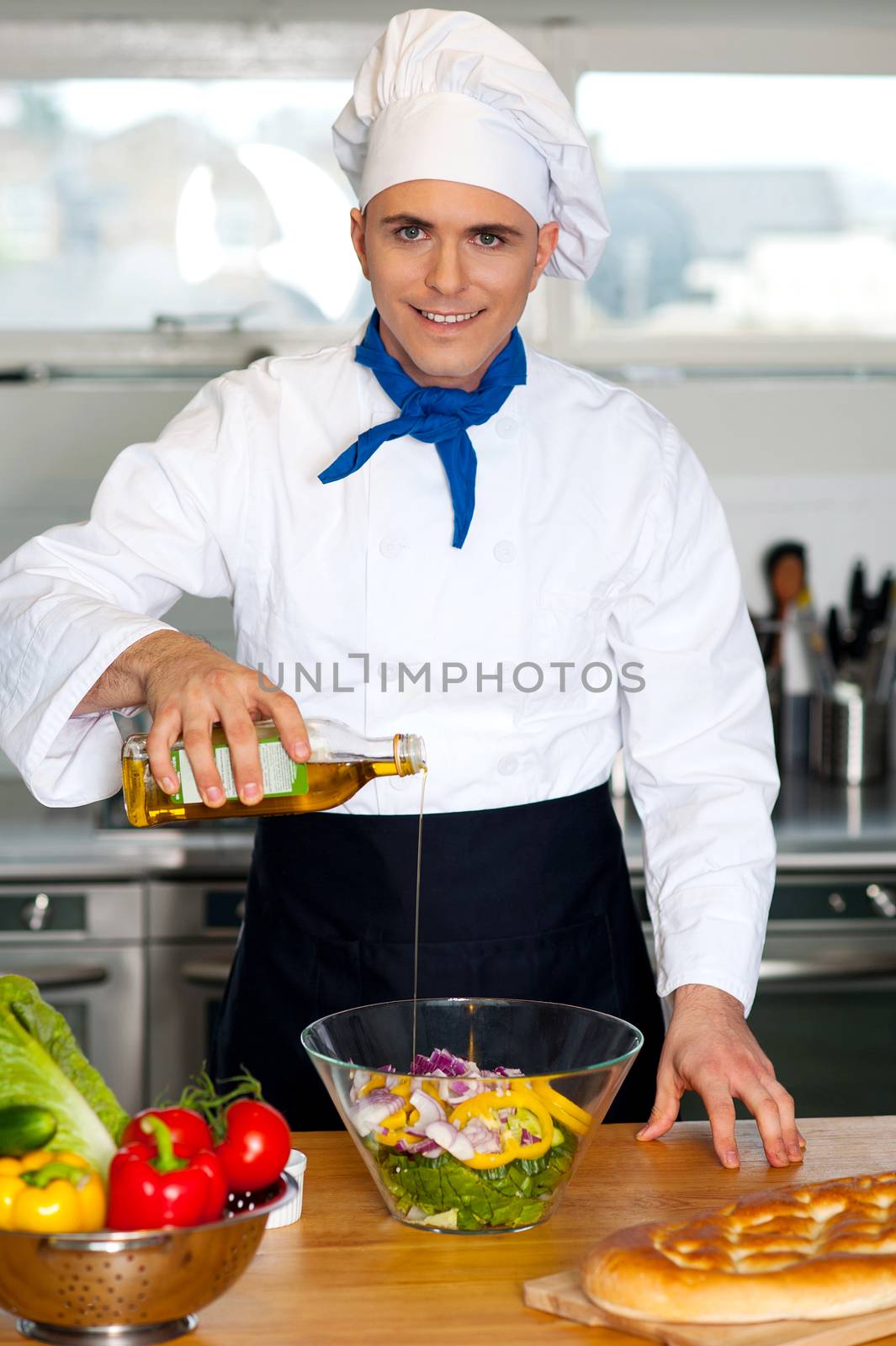 Image of male chef pouring oil into vegetable salad in the kitchen