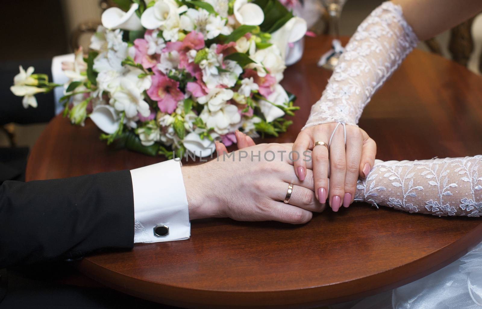 hands of the bride and groom and wedding flowers on the table.