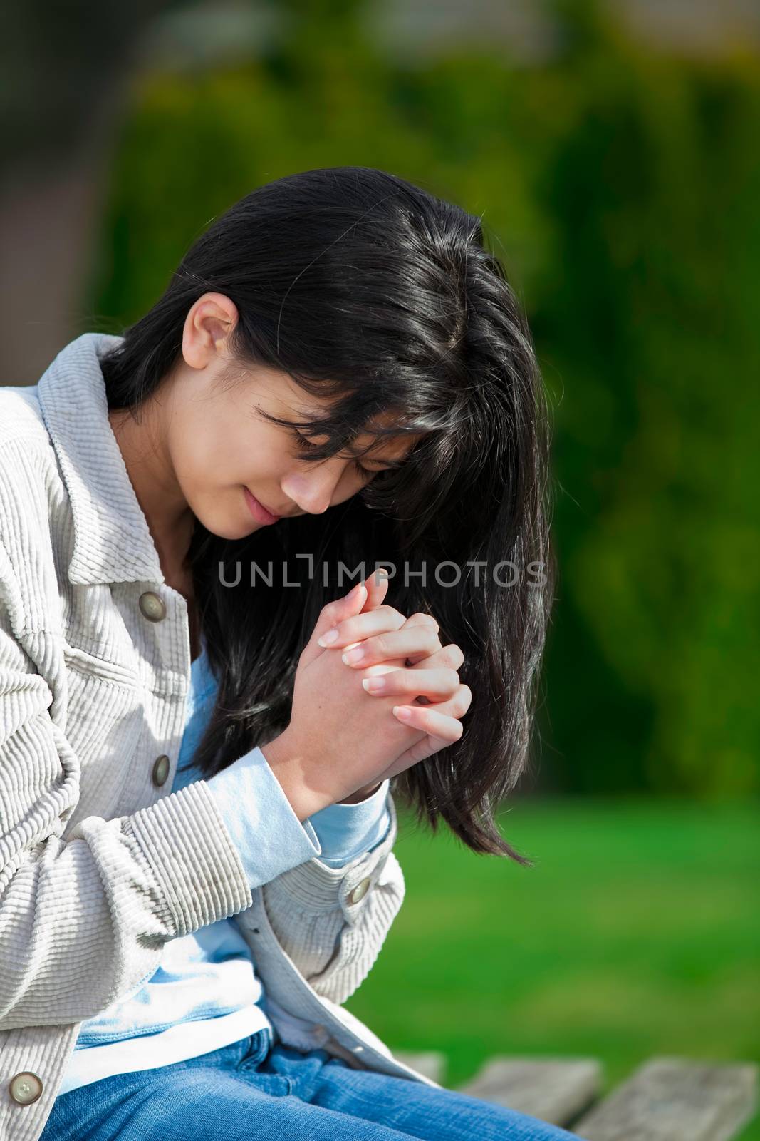Young biracial teen girl praying outdoors on bench by jarenwicklund