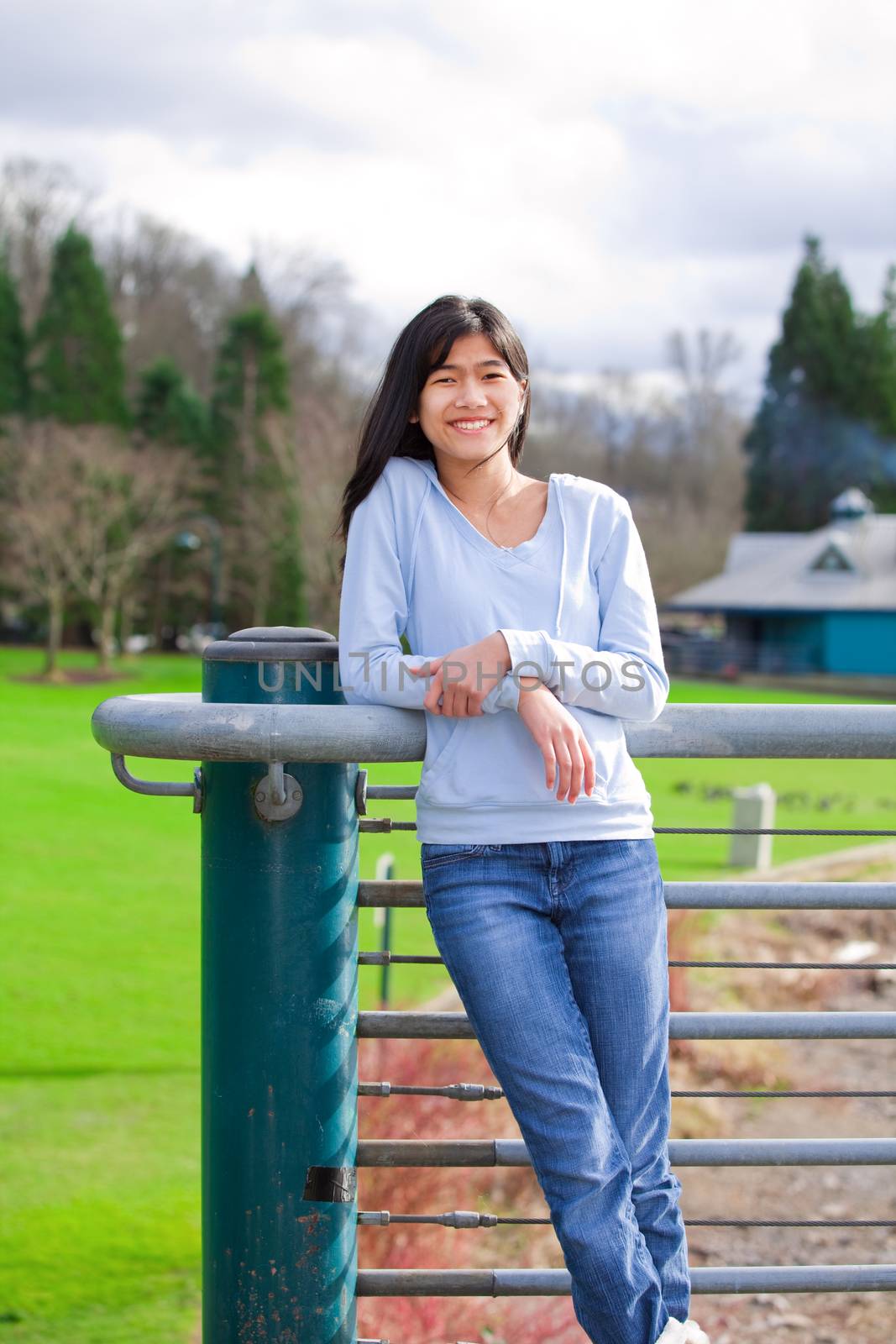 Young teen girl standing, leaning against railing at park by jarenwicklund