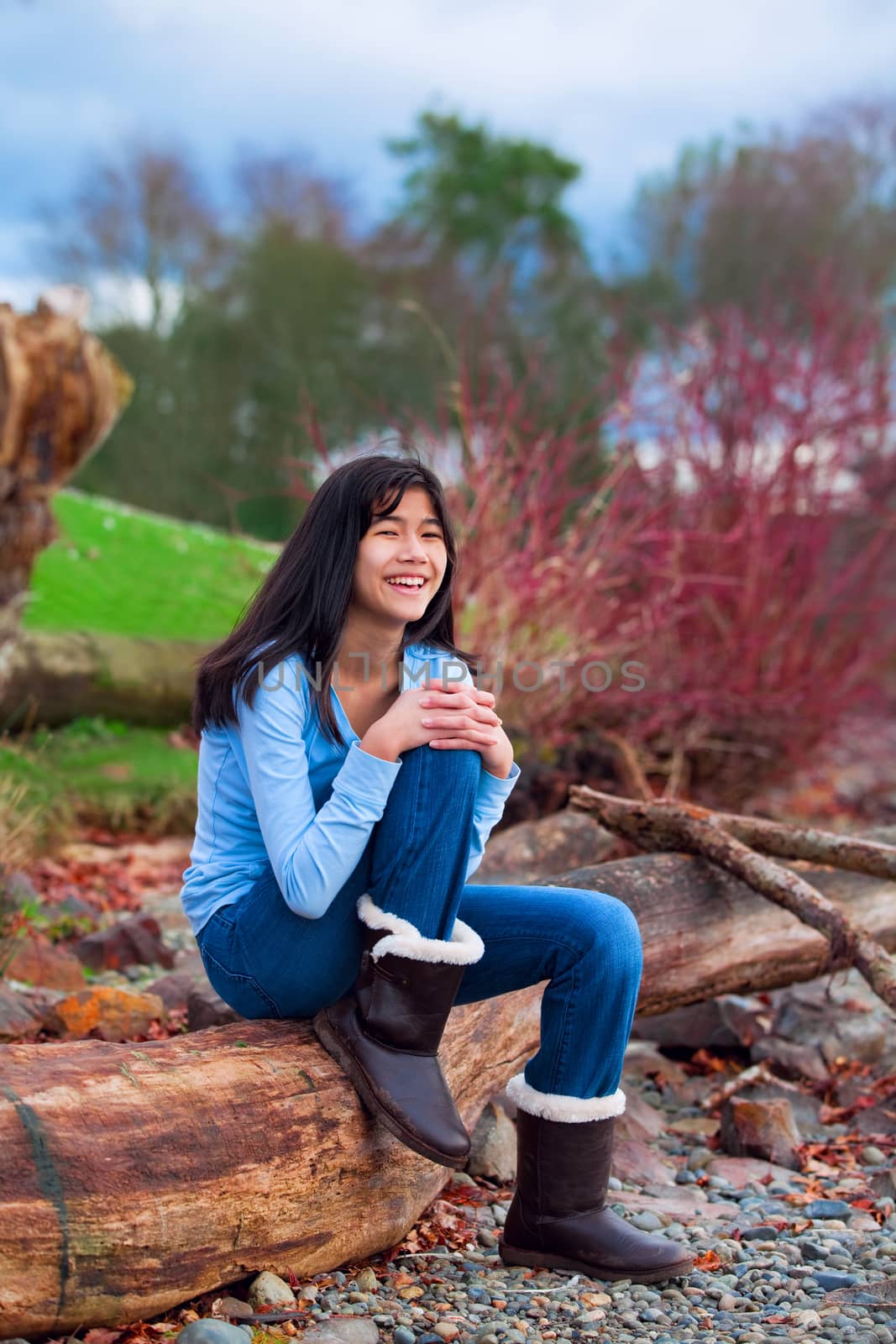 Young teen girl sitting on log along rocky beach of lake by jarenwicklund