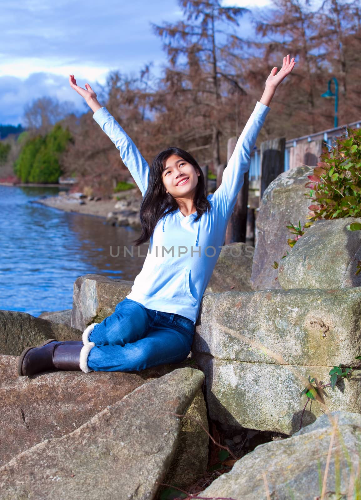 Young teen girl arms raised while sitting on large rock along la by jarenwicklund