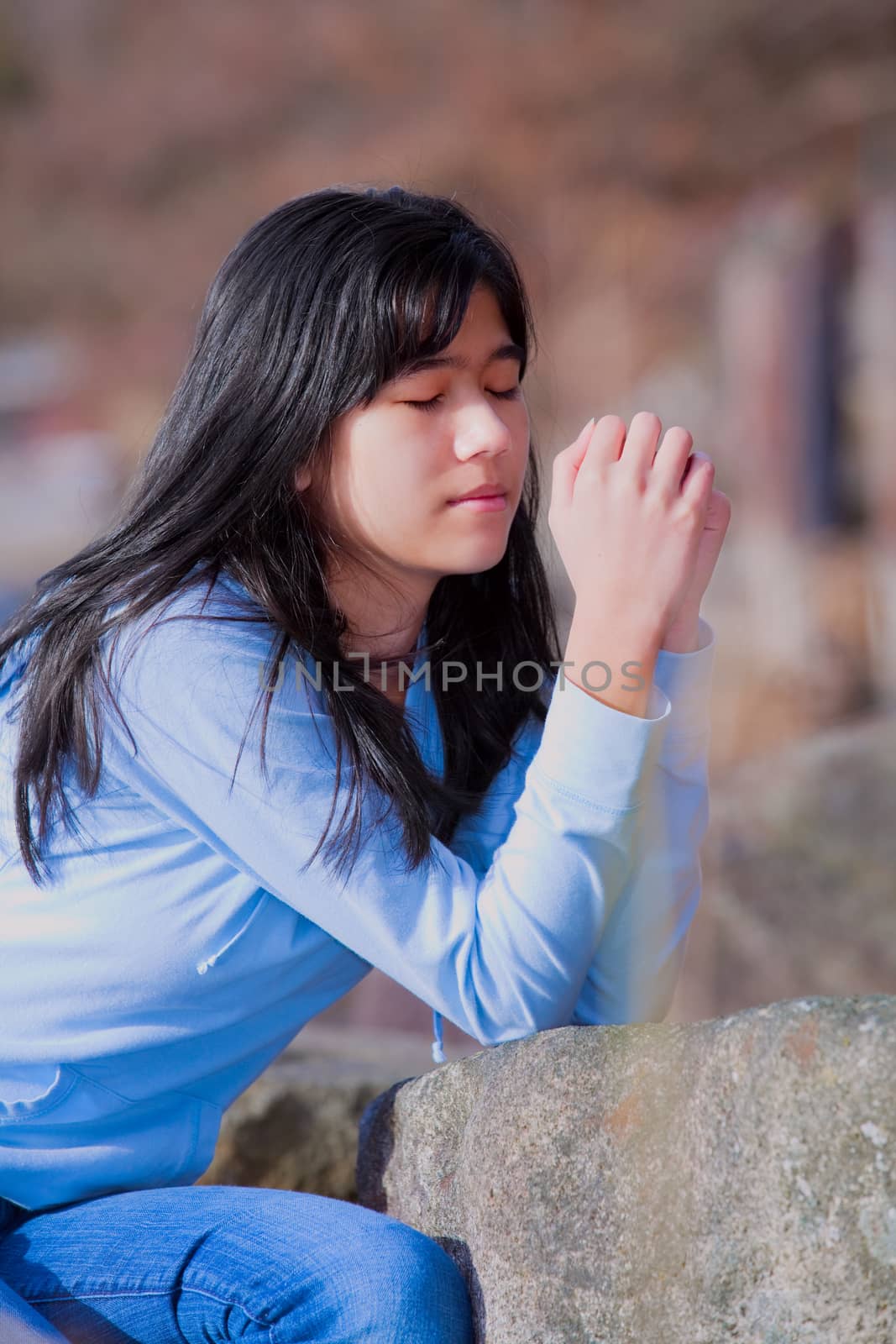 Young teen girl sitting outdoors on rocks praying by jarenwicklund