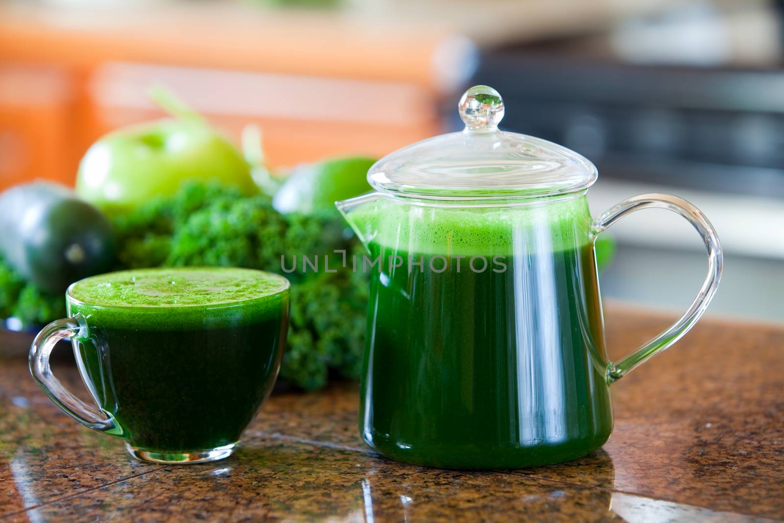 Glass cup of green vegetable juice on kitchen counter, made with kale, spinach, lime, apple, cucumber.