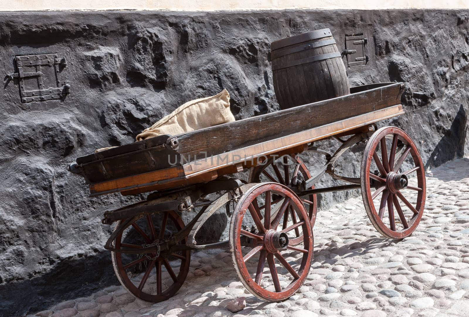 old wooden cart  with a bag and a barrel on background of old brick wall