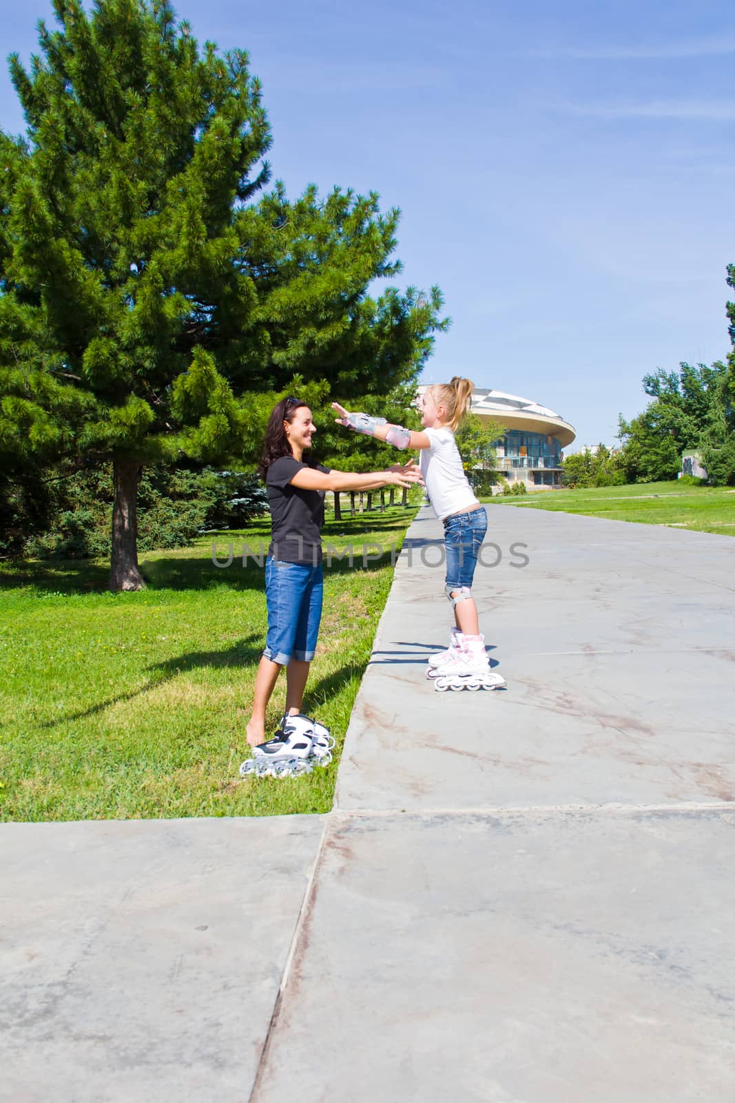 Learning mother and daughter on roller skates in summer