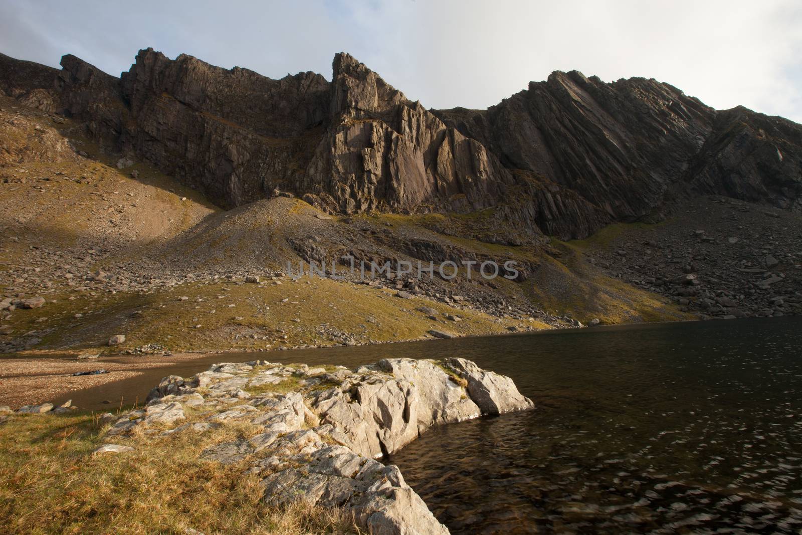 A rocky foreground leads to a lake and the impressive mountain crags of Clogwyn Du'r Arddu, Snowdonia national park, Wales, UK.