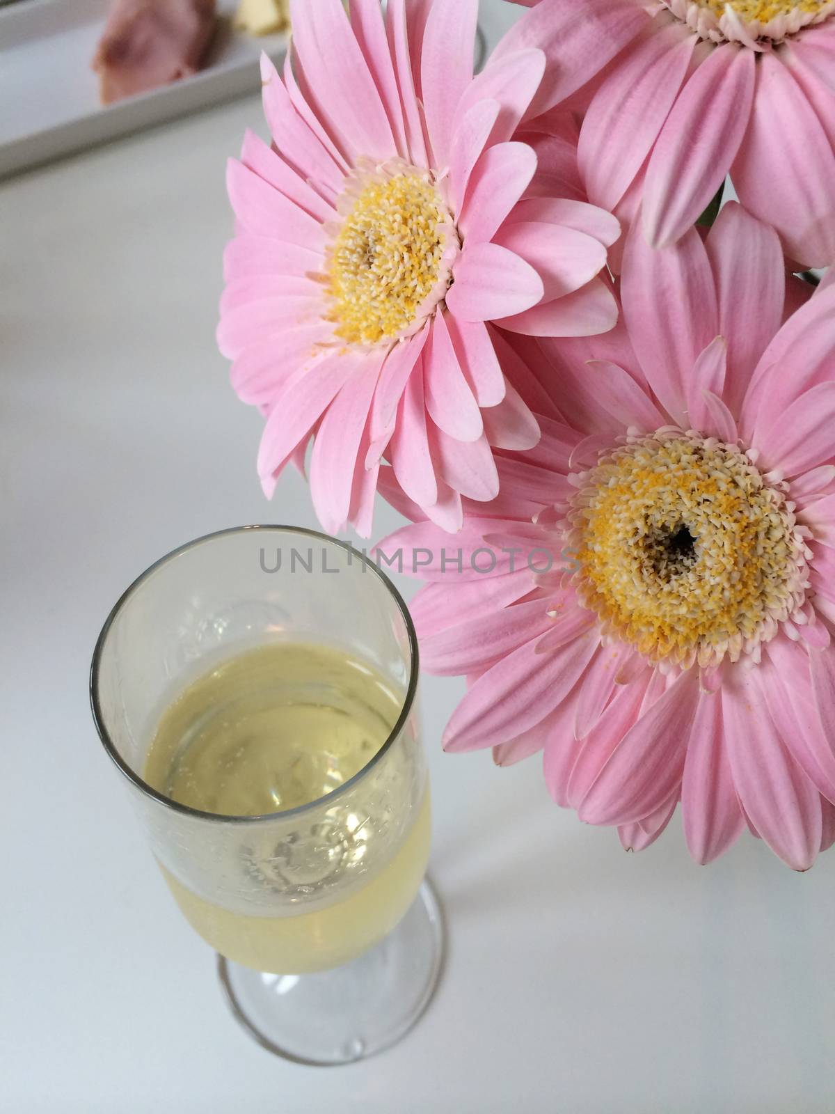 A glass of champagne and pink daisies on a white surface 