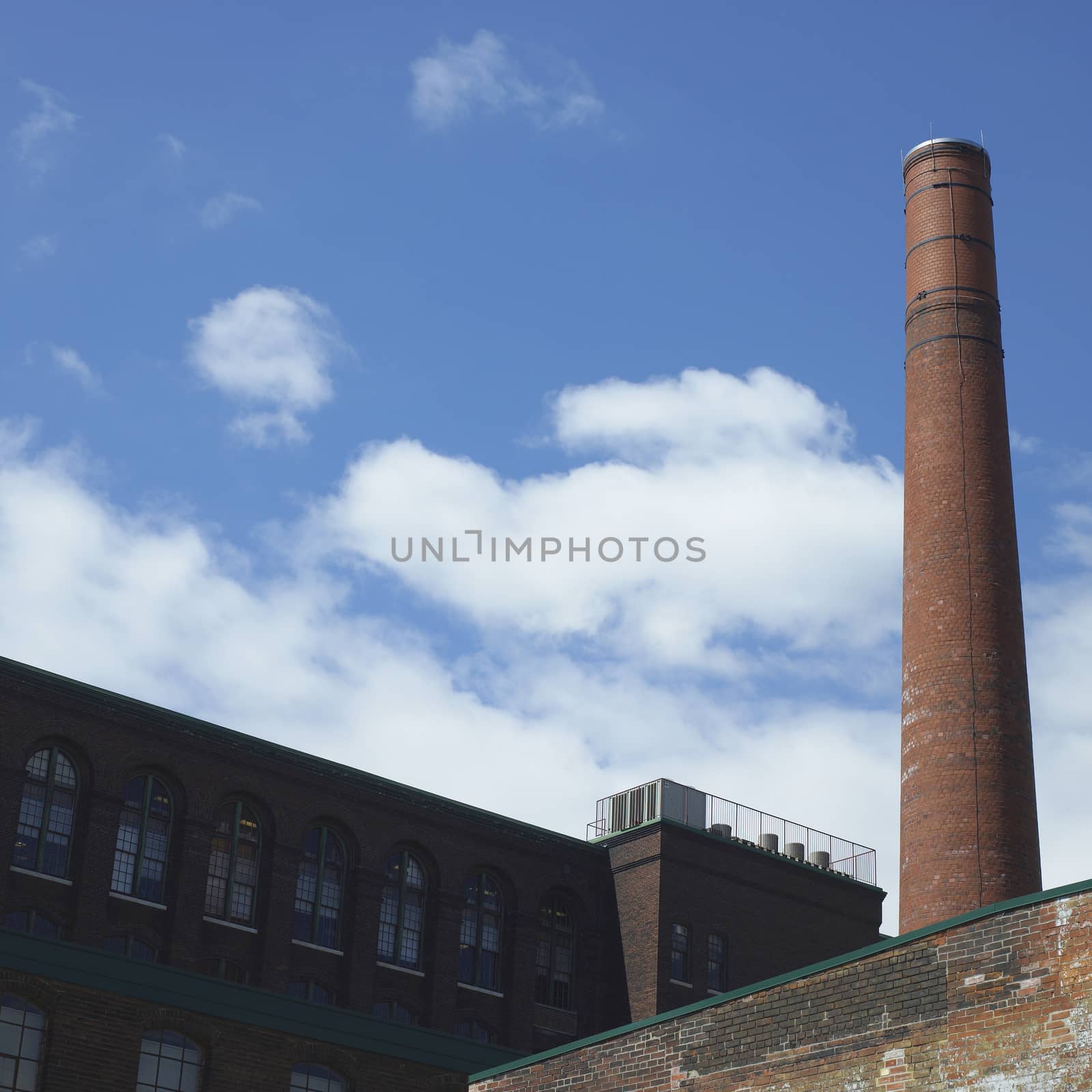 Towering brick smoke stack inside the walls of a large old factory 