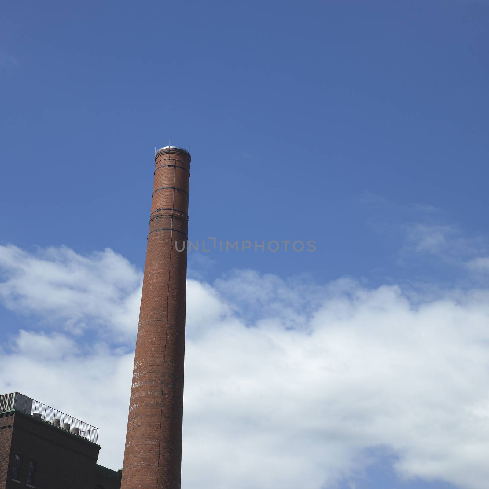 Tall brick smoke stack and factory wall against a blue sky
