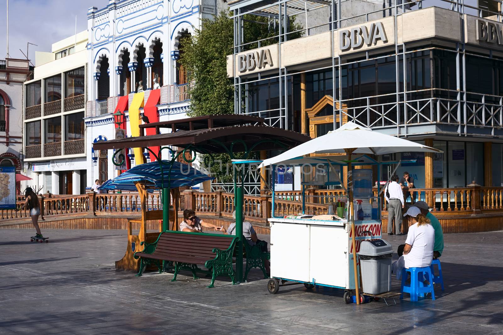 IQUIQUE, CHILE - JANUARY 22, 2015: Unidentified people sitting at Mote con Huesillo (Chilean cold drink) stand on Plaza Prat main square with the building of BBVA bank and the Casino Espanol next to it on January 22, 2015 in Iquique, Chile