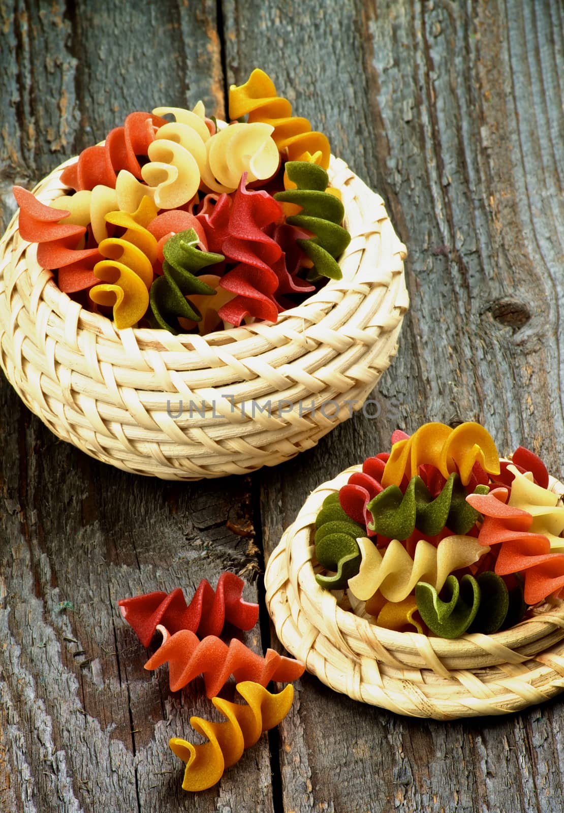 Multi Colored Rotini Pasta in Wicker Bowls closeup on Rustic Wooden background