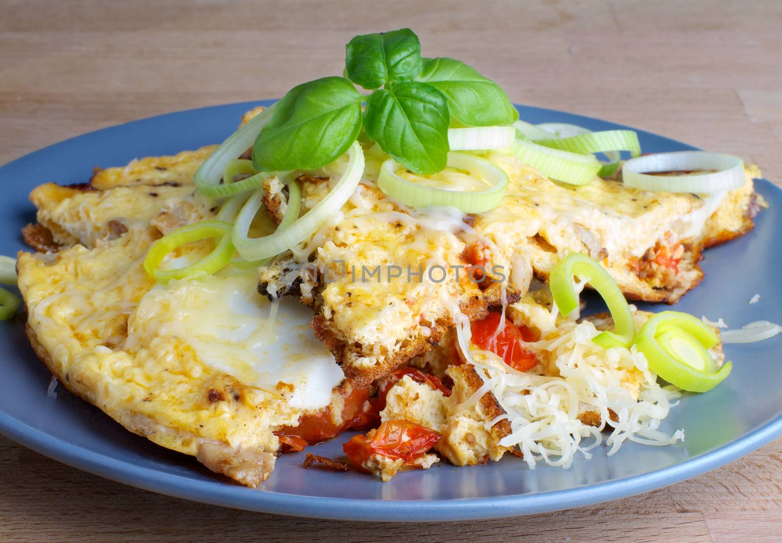 Tasty Omelette with Tomatoes, Leek and Grated Cheese on Grey Plate closeup on Wooden background