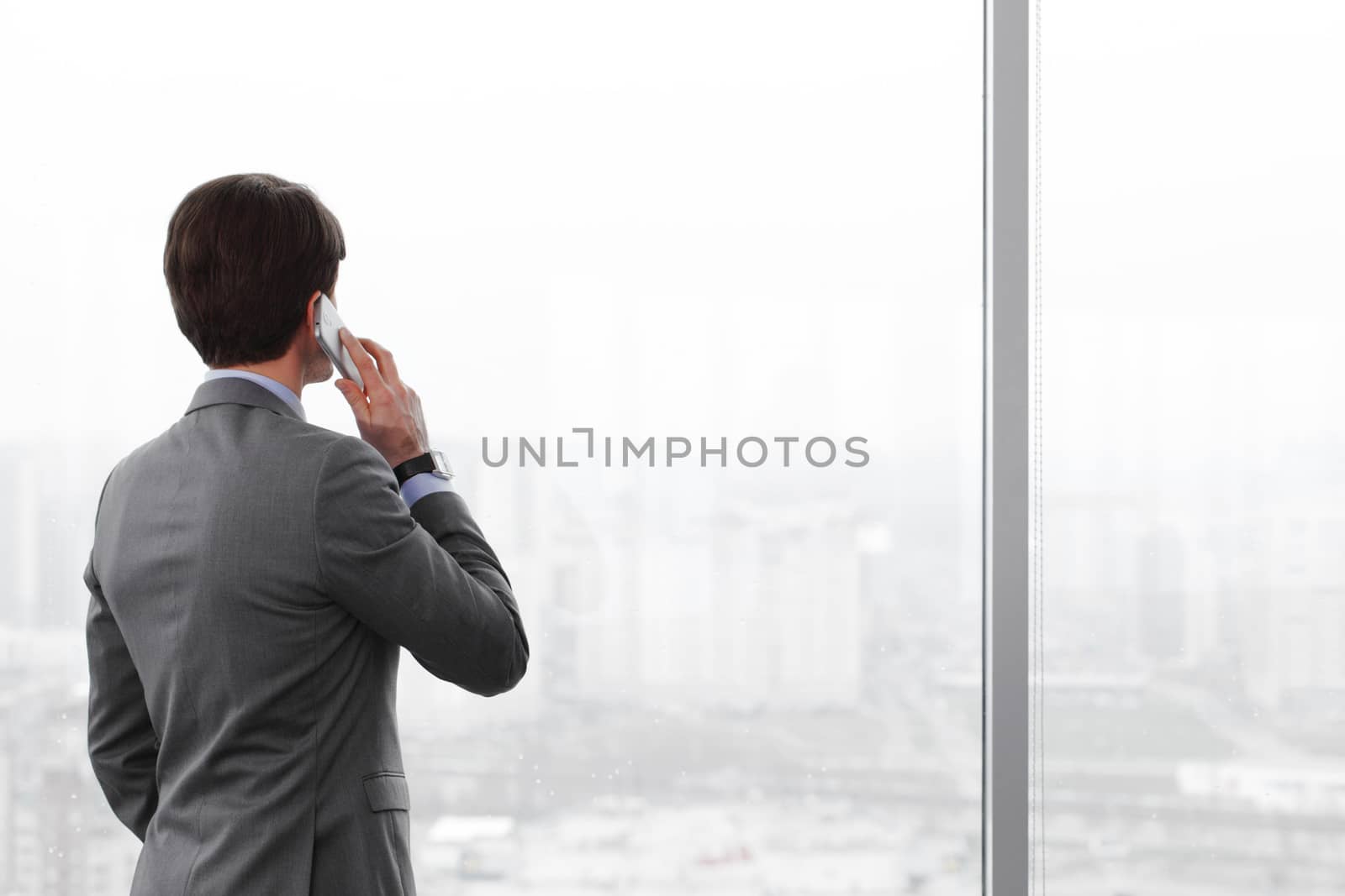 businessman with mobile phone looking through window