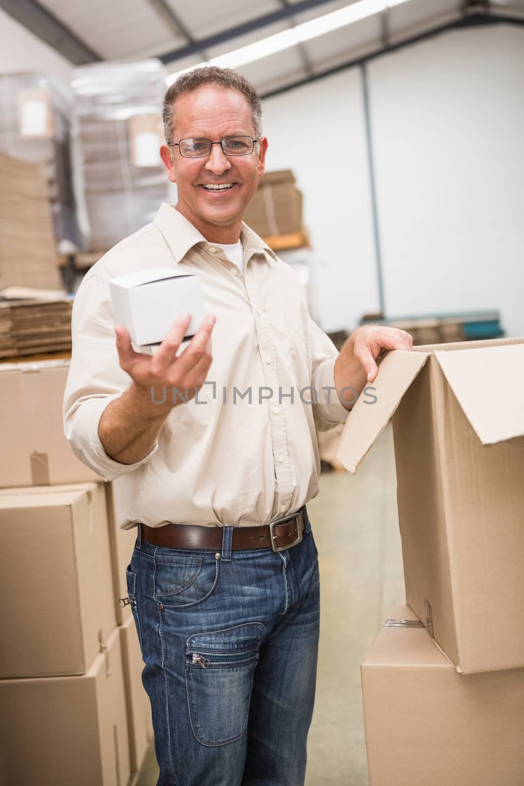 Smiling warehouse worker holding small box in a large warehouse