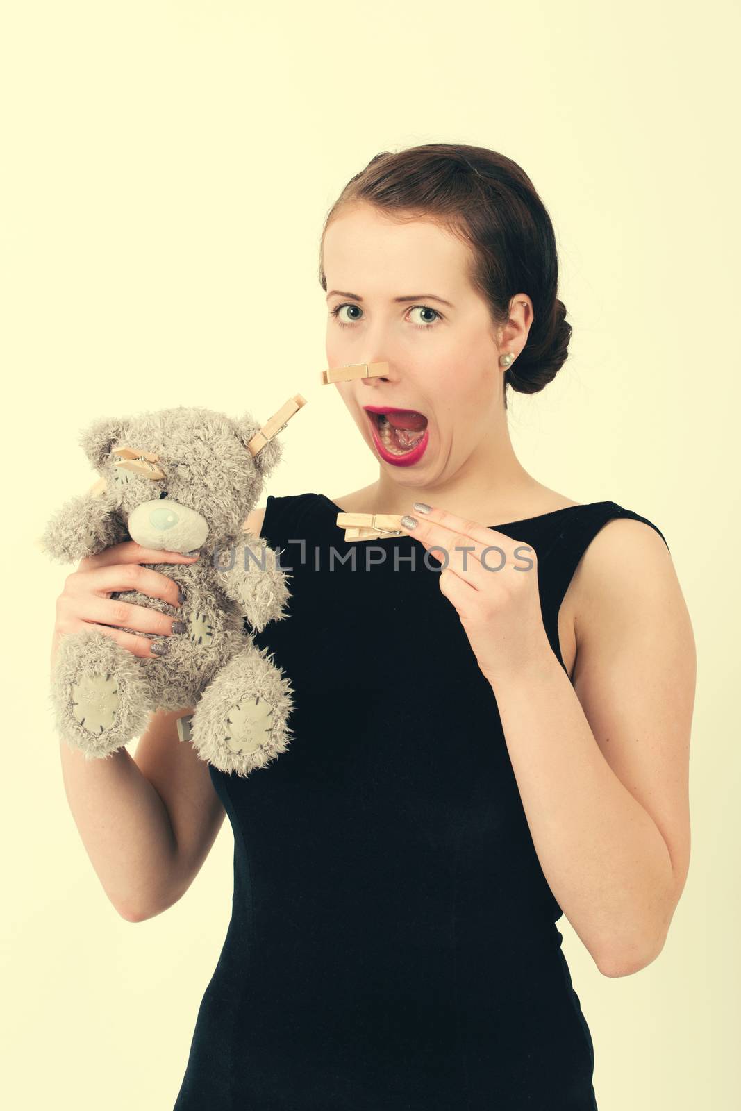 attractive smiling brunette holding teddy bear grimacing with peg on nose in a black dress, retro color