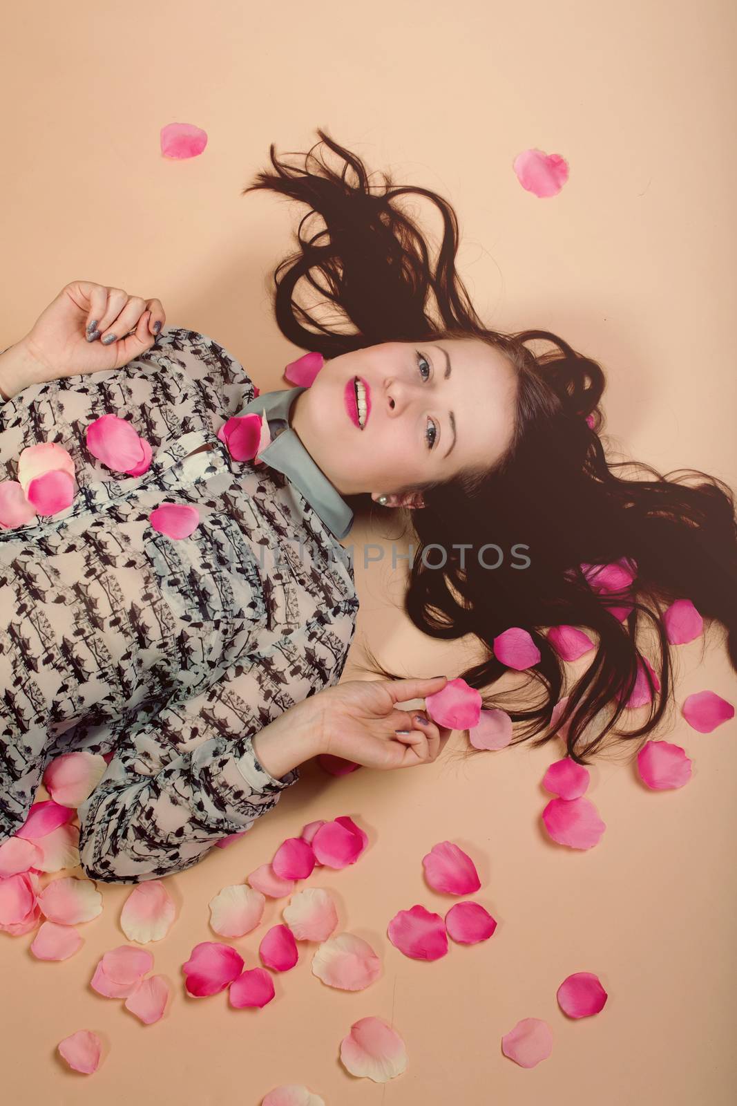 atractive brunette girl lying on beige background, with rose petals around. Beaty concept.