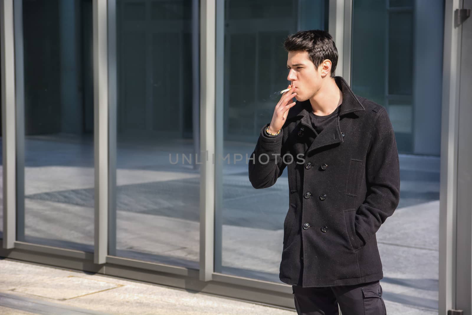 Handsome stylish young man smoking outside in urban setting, looking away