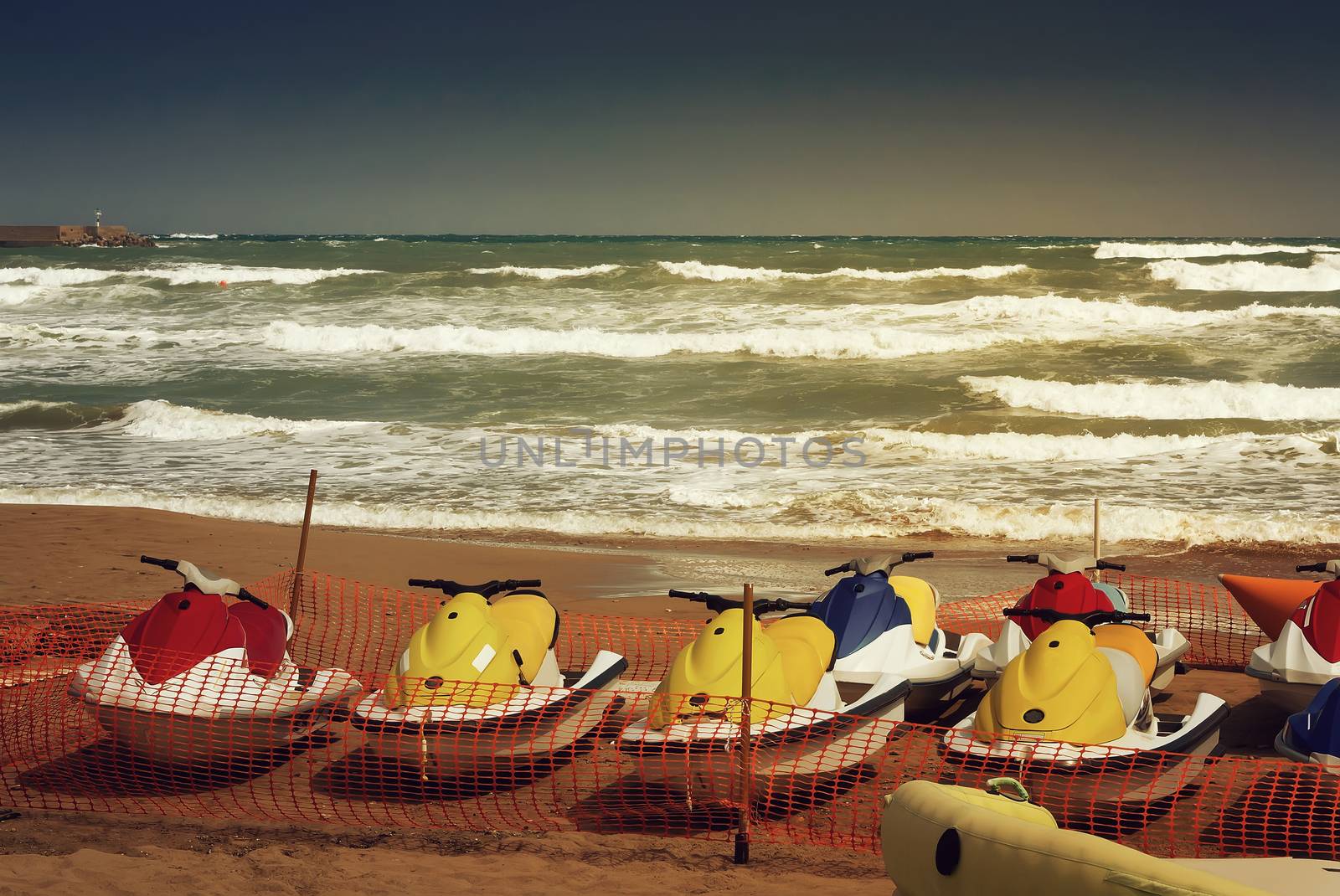 On the beach in the fenced area there are water scooters that are not used because of the storm on the sea.