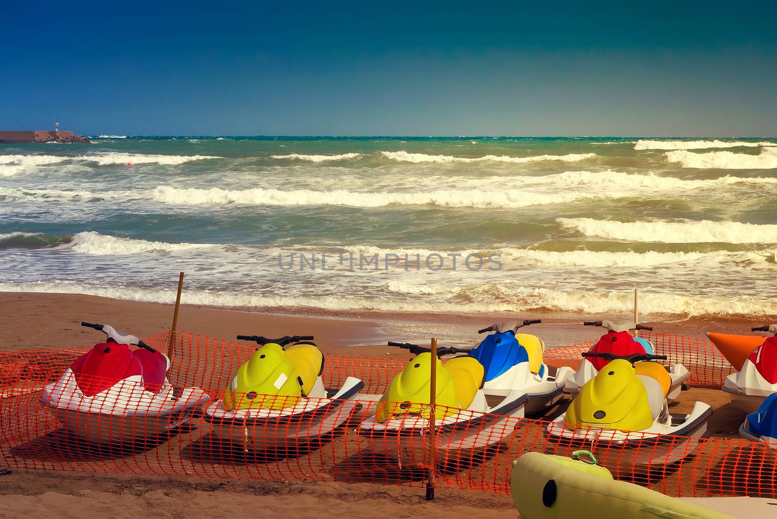 On the beach in the fenced area there are water scooters that are not used because of the storm on the sea.